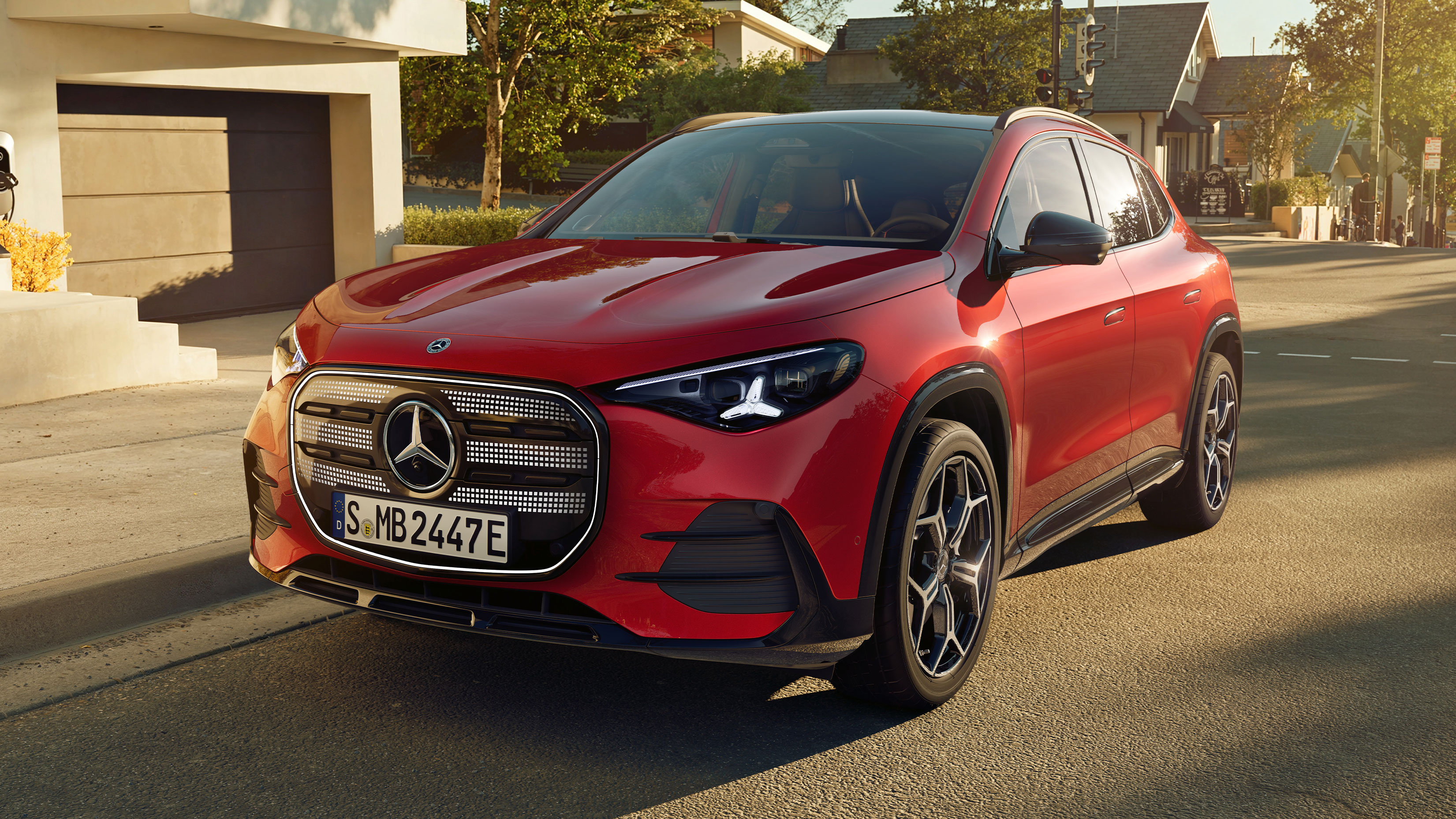 GLA | Mercedes-Benz Der neue elektrische GLA in Rot in seitlicher Frontalansicht steht auf einer Straße in einer Wohnsiedlung.