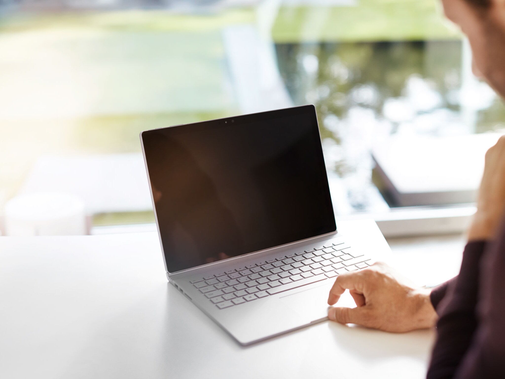 Ein Mann sitzt an seinem Schreibtisch und schaut auf seinen Laptop in einem hellen Raum.