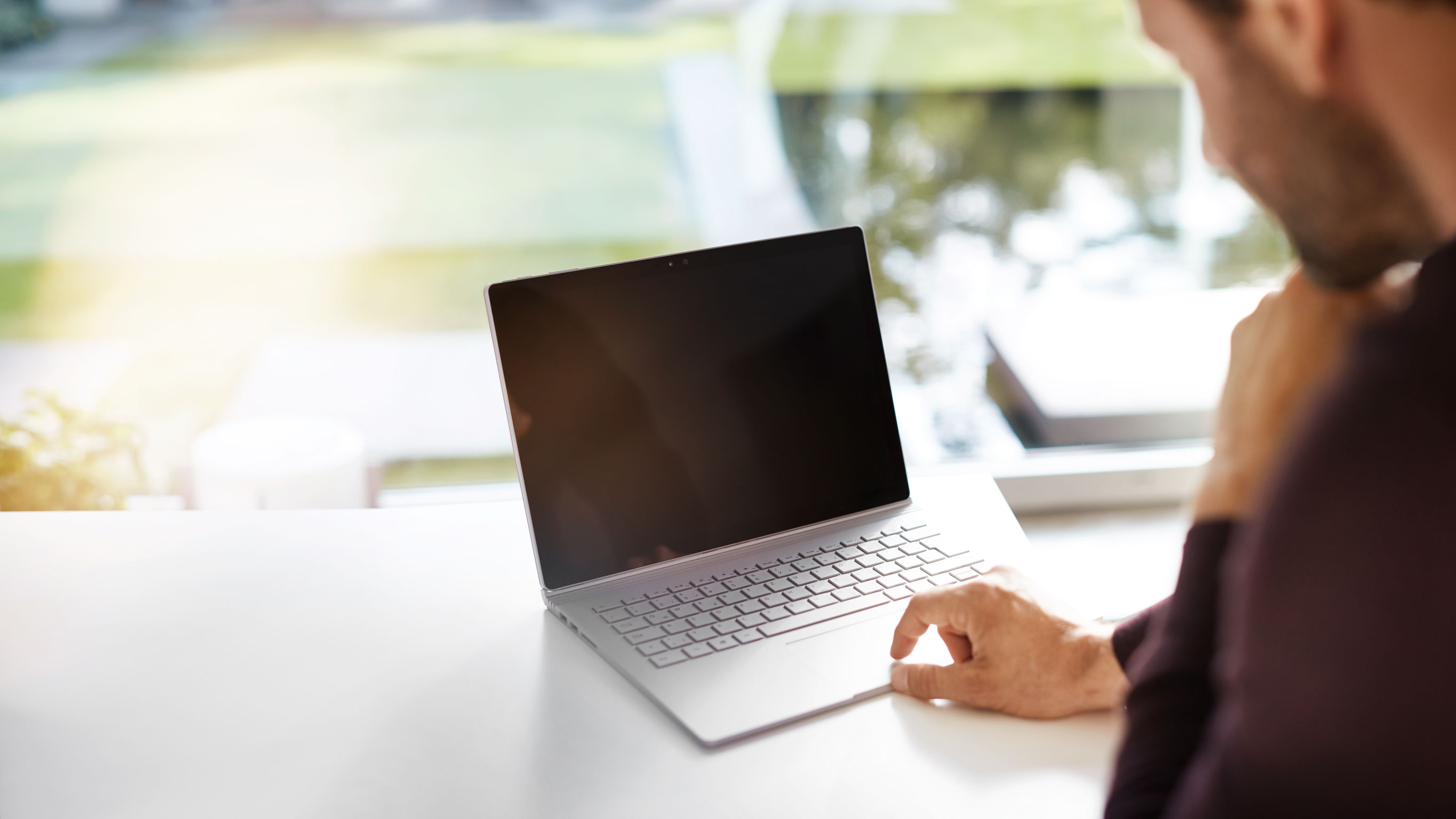 Neuwagen kaufen - so geht's! | Mercedes-Benz Ein Mann sitzt an seinem Schreibtisch und schaut auf seinen Laptop in einem hellen Raum.