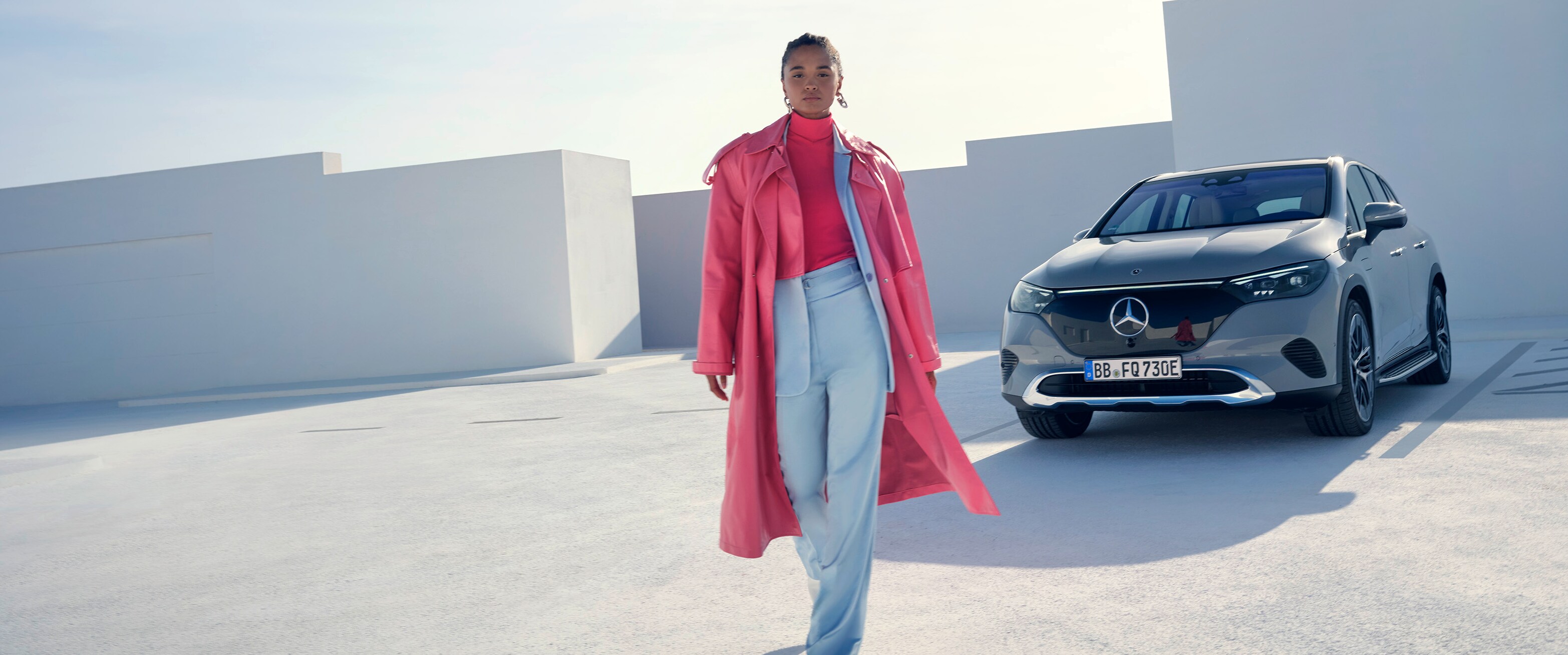 Eine Frau in einem rosafarbenen Outfit geht von ihrem Fahrzeug von Mercedes-Benz weg.