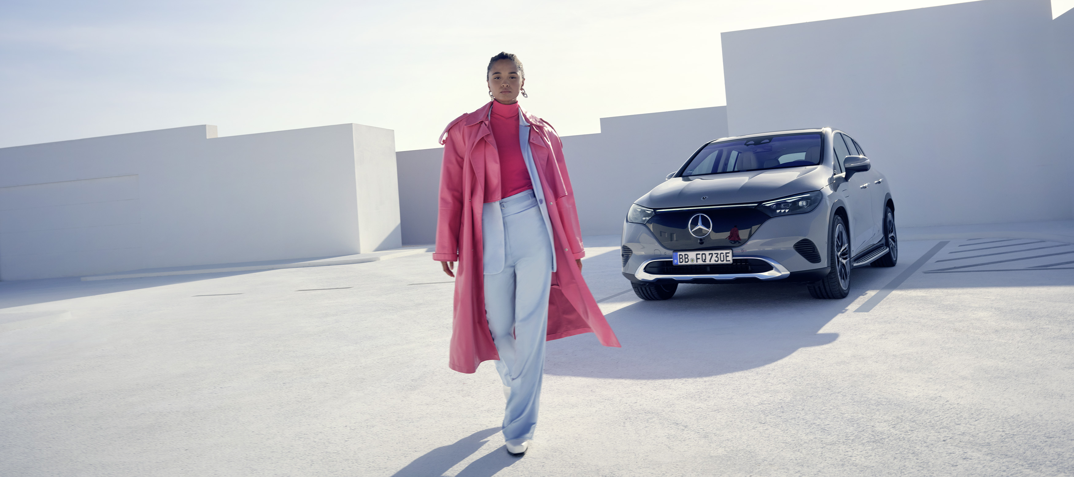 Sicherheit & GUARD 360° | Digitale Extras | Mercedes-Benz Eine Frau in einem rosafarbenen Outfit geht von ihrem Fahrzeug von Mercedes-Benz weg.