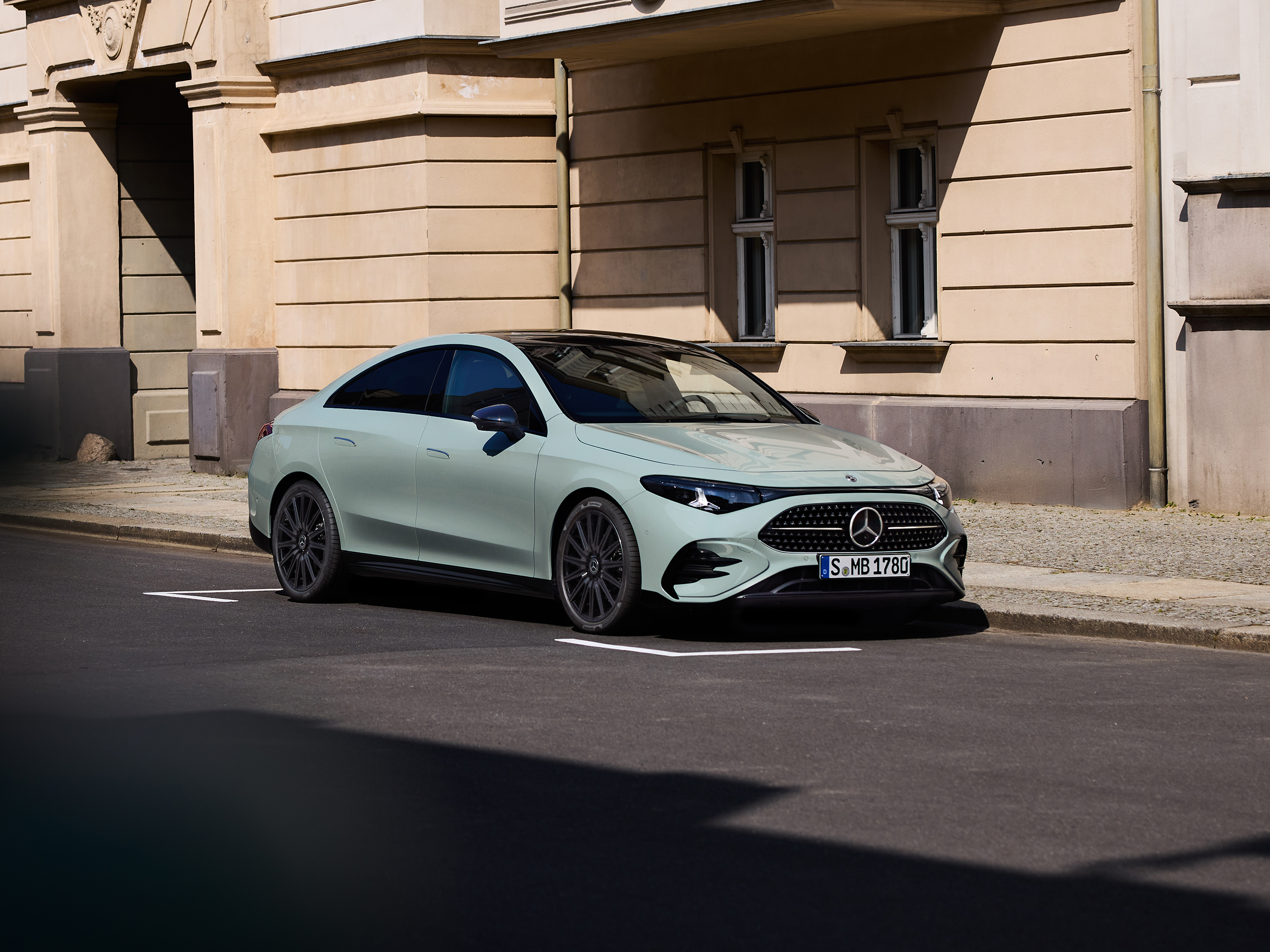 Aktuelle Online-Aktionen | Mercedes-Benz. Eine CLA Limousine in Aquamint vor einem sandfarbenen Gebäude in Potsdam.