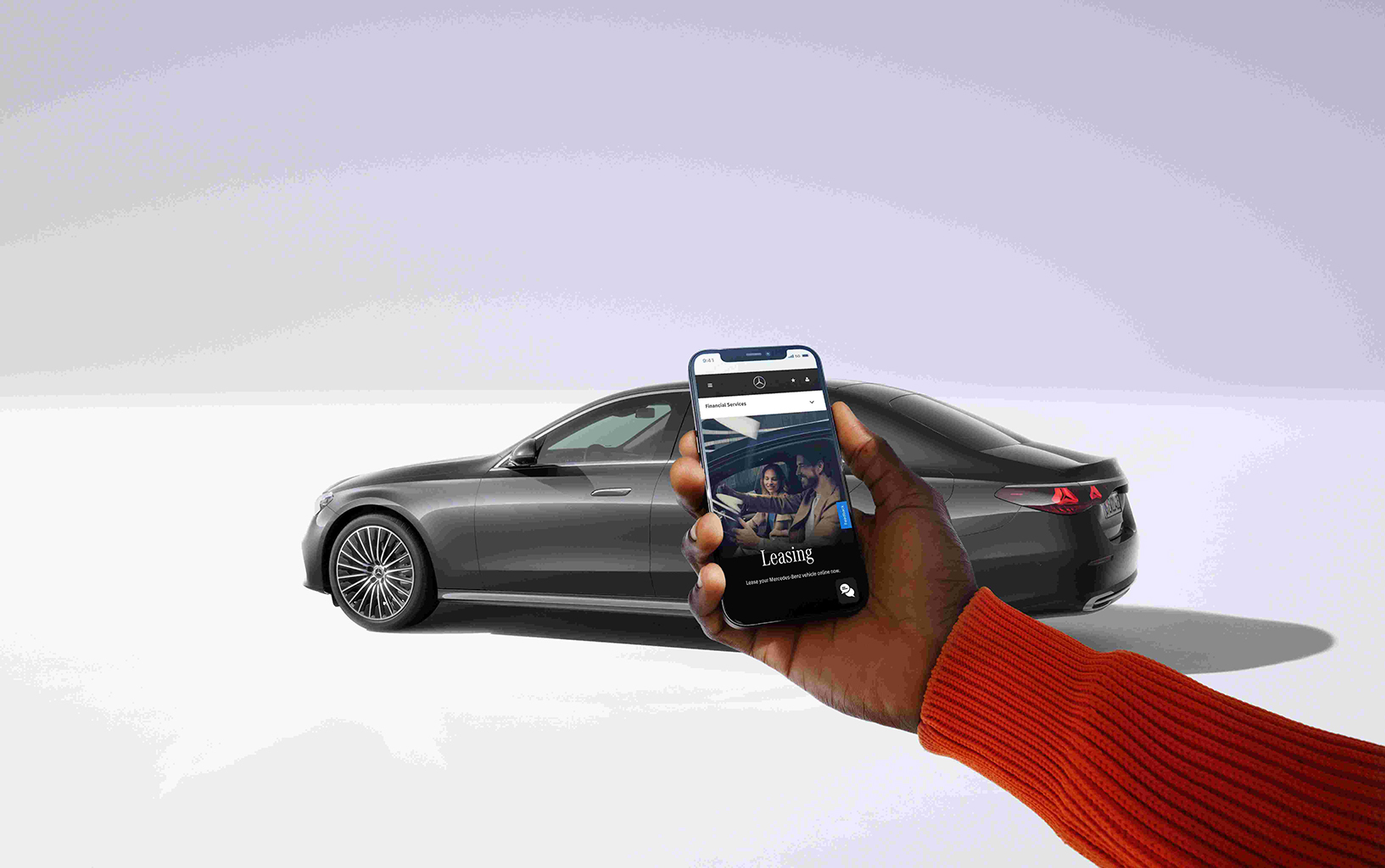 Neuwagen kaufen - so geht's! | Mercedes-Benz Ein Auto von Mercedes-Benz im Hintergrund. Davor eine Person mit Handy in der Hand auf dem ein Leasingangebot zu sehen ist.