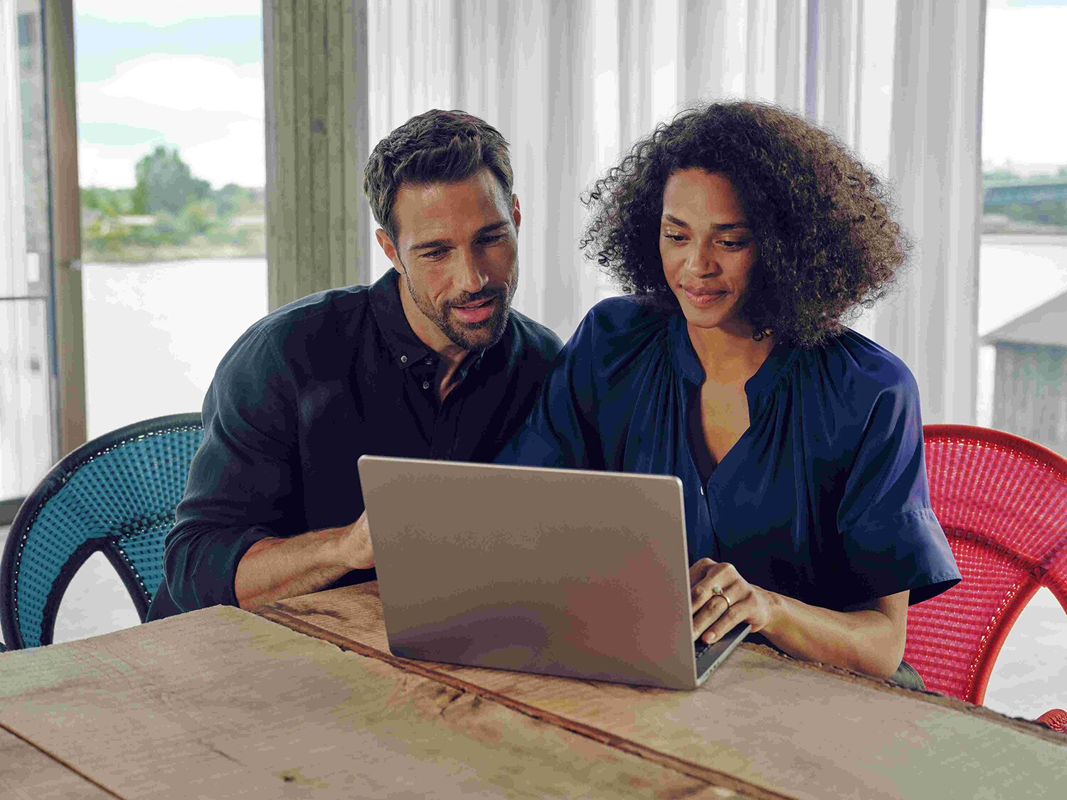 Ein Mann und eine Frau sitzen an einem Tisch und schauen aufmerksam auf einen Laptop.