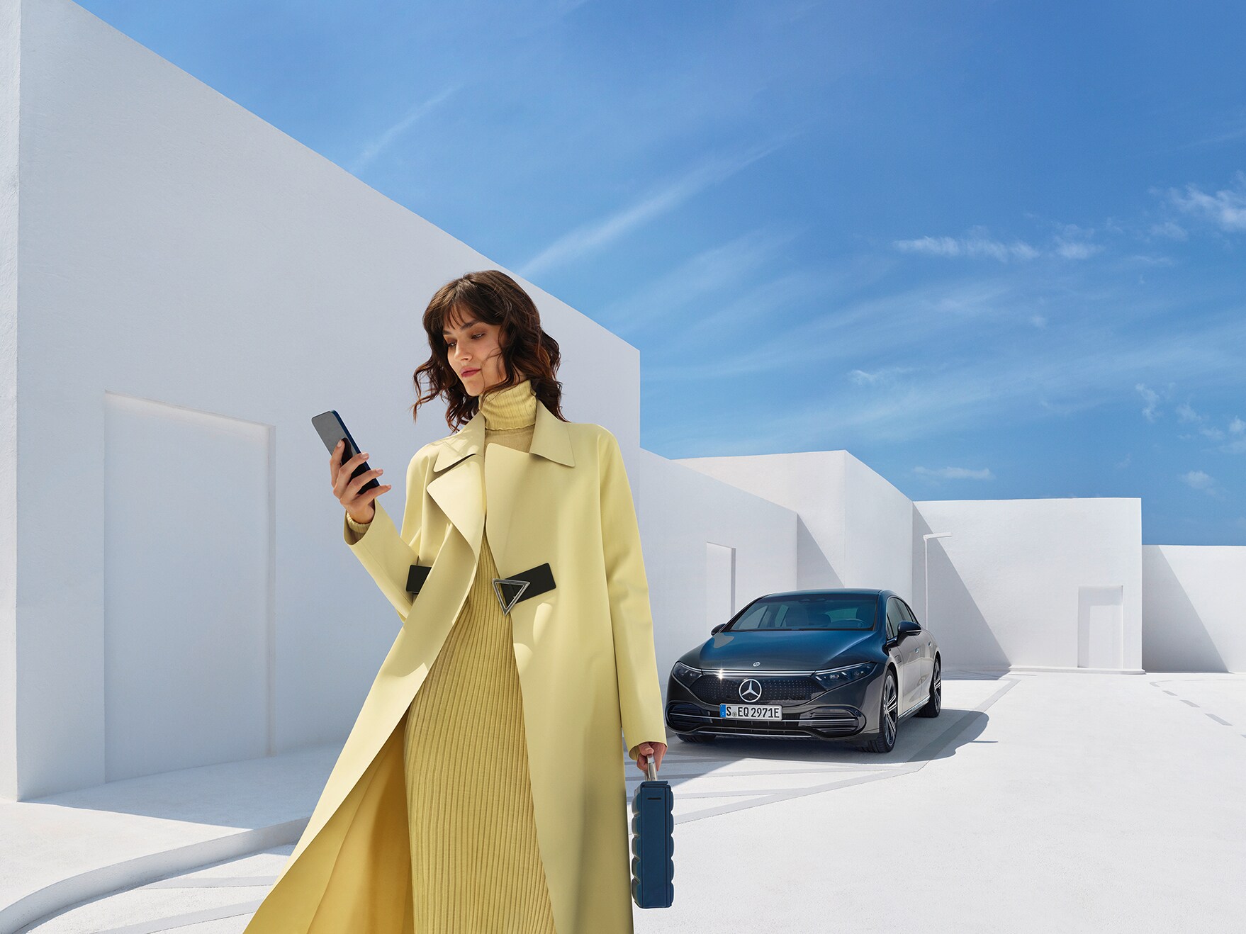 Eine Frau in gelbem Outfit schaut auf ihr Handy und steht dabei an einem Straßenrand.