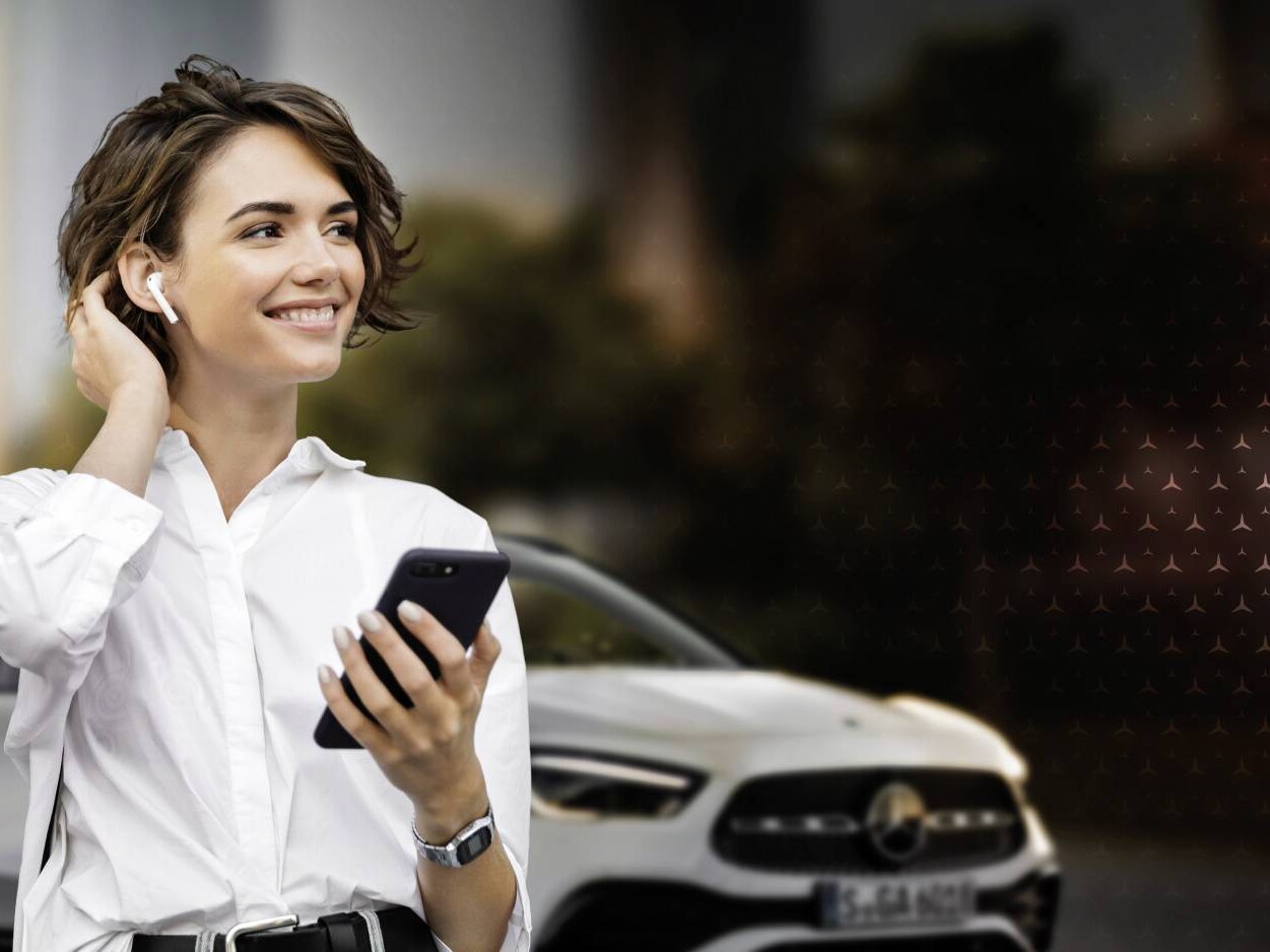 Eine Frau mit Bluetooth-Kopfhörer und Handy lächelt in die Ferne.