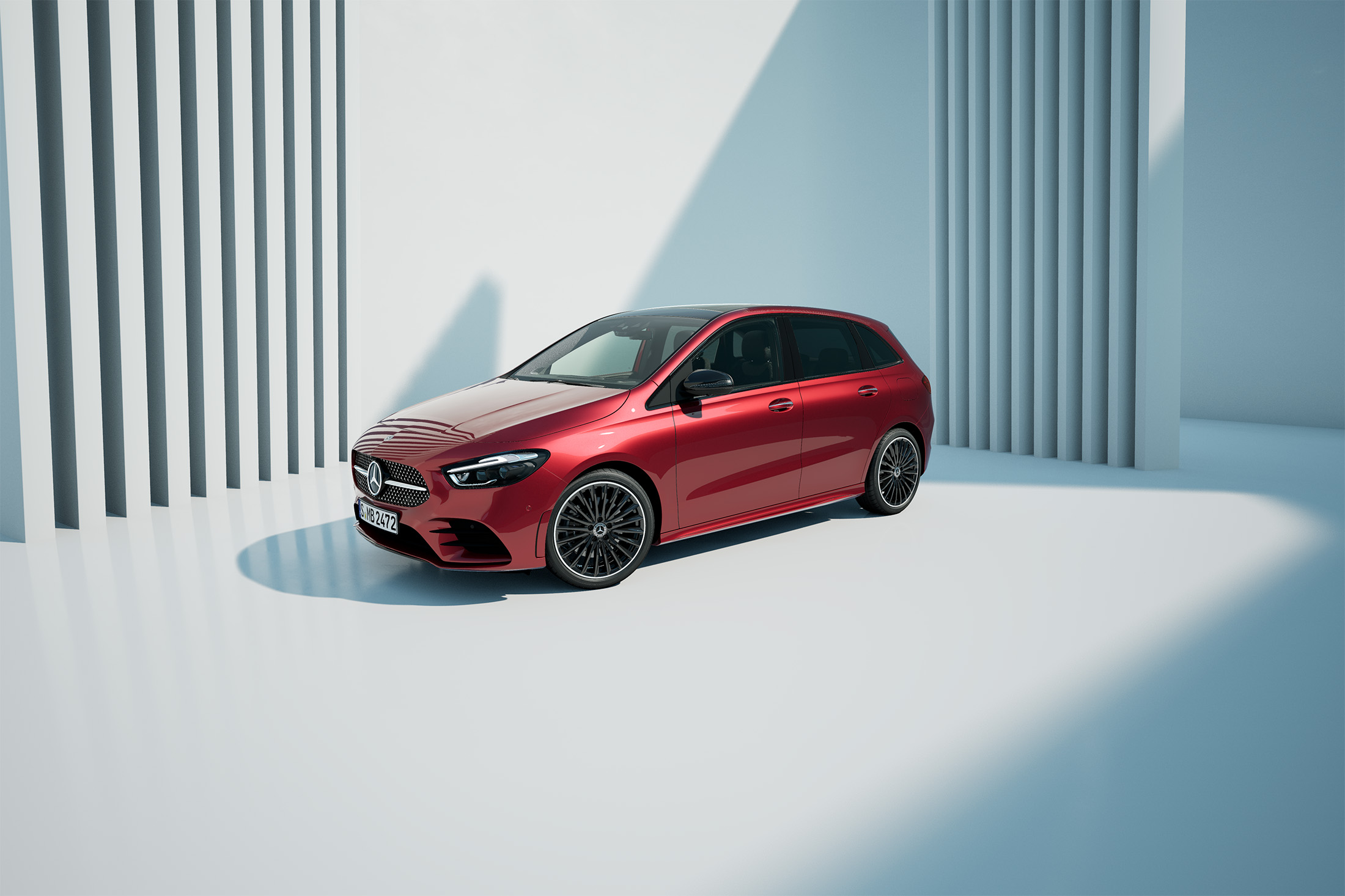 Aktuelle Online-Aktionen | Mercedes-Benz. Eine rote B-Klasse auf hellem Grund vor einer Wand mit Lamellen.