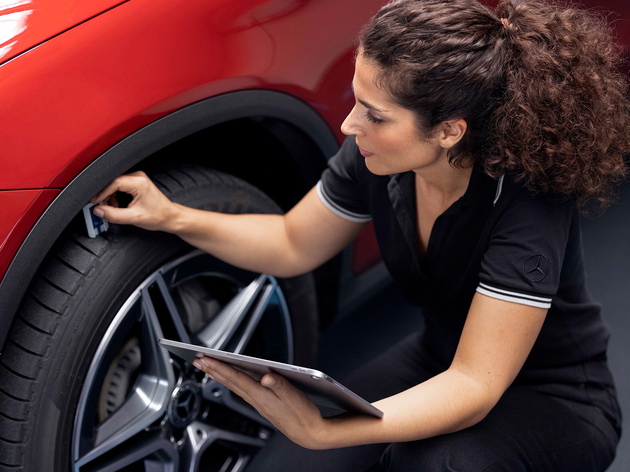 Eine Mercedes‑Benz Servicemitarbeiterin überprüft die Profiltiefe an einem Vorderrad.