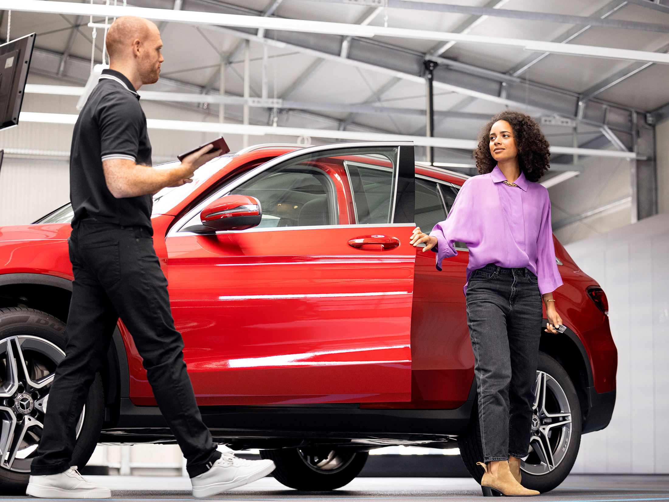 Service Plan Reifen Eine Frau übergit in der Werkstatt ihren roten Mercedes-Benz einem Servicemitarbeiter.