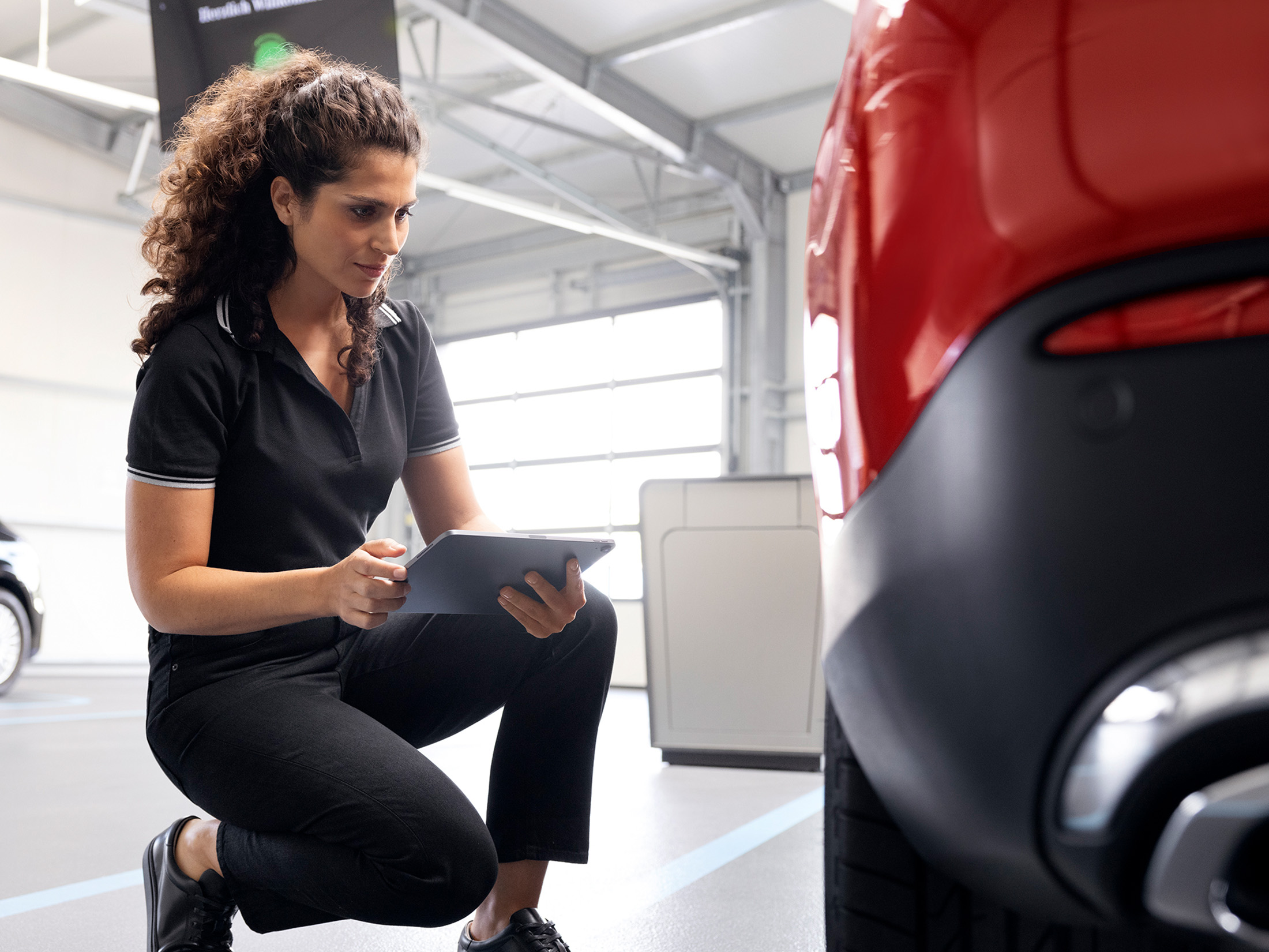 Service Plan Reifen Premium Eine Mercedes-Benz Servicemitarbeiterin checkt geht knieend neben einem Mercedes-Benz auf iihrem Laptop eine Checkliste durch.