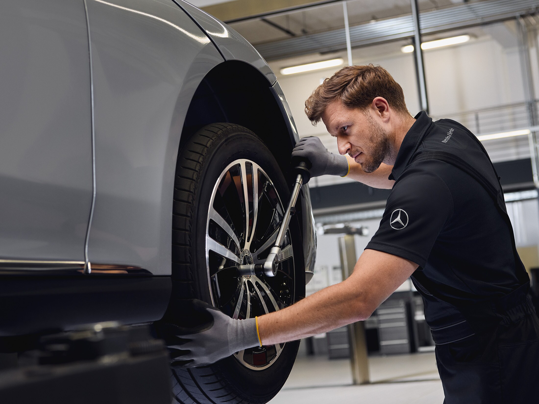 Ein Mercedes‑Benz Mechaniker montiert in der Werkstatt ein Vorderrad auf einer Hebebühne.