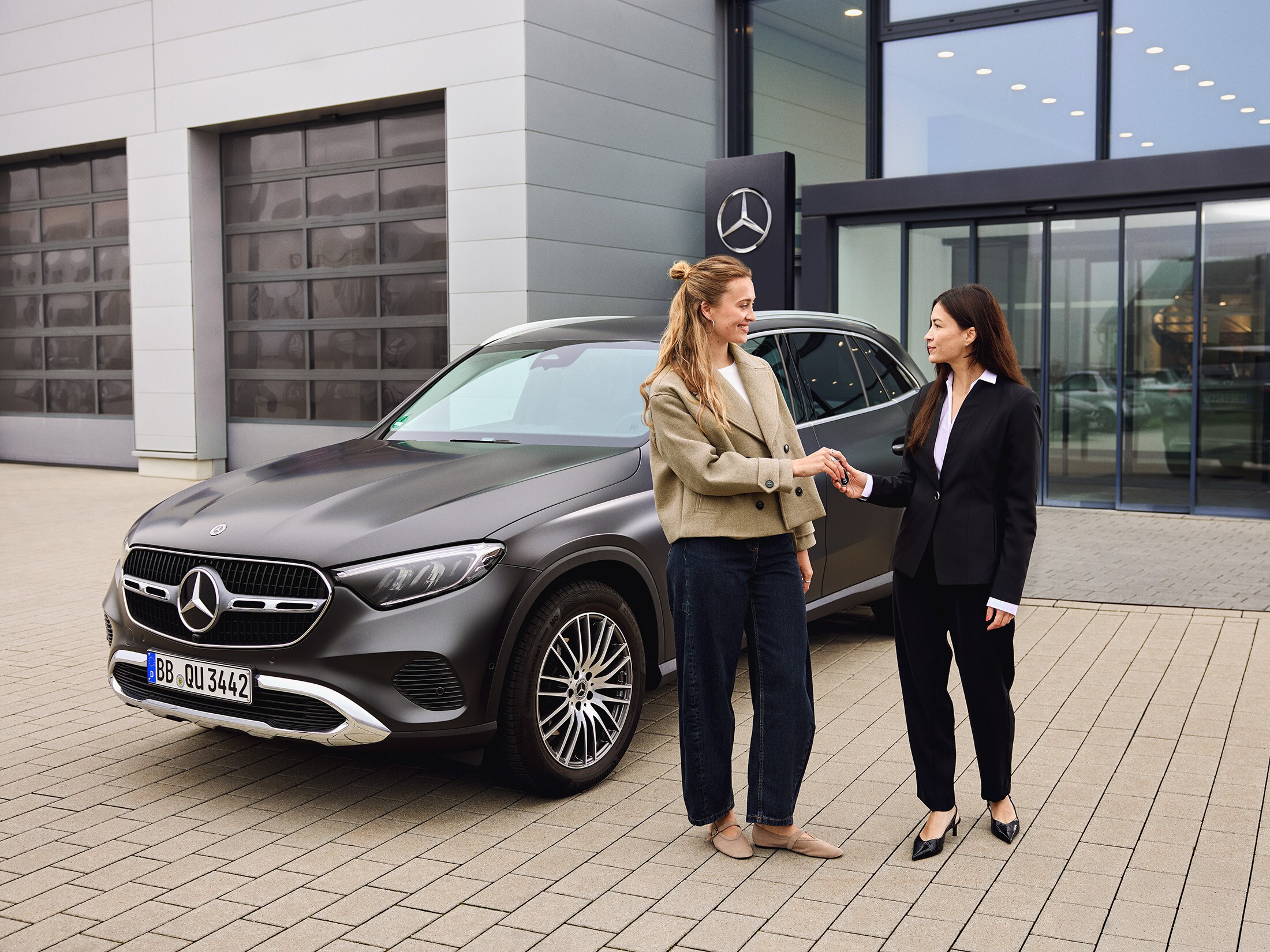 Eine Frau übergibt vor einem Mercedes-Benz ihre Autoschlüssel an eine Servicemitarbeiterin.