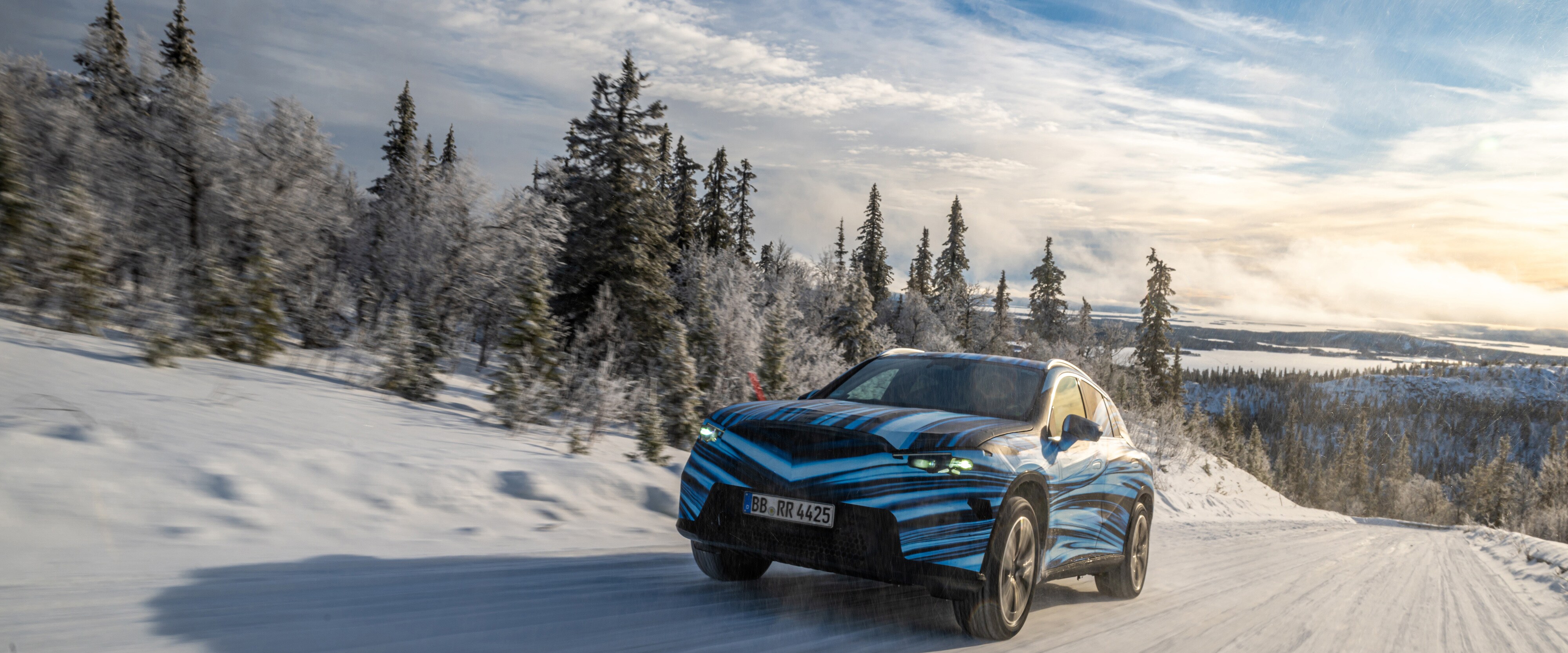 Der neue GLC BEV beklebt mit Folie, fährt in einer Schneelandschaft mit Bäumen und blauen Himmel.