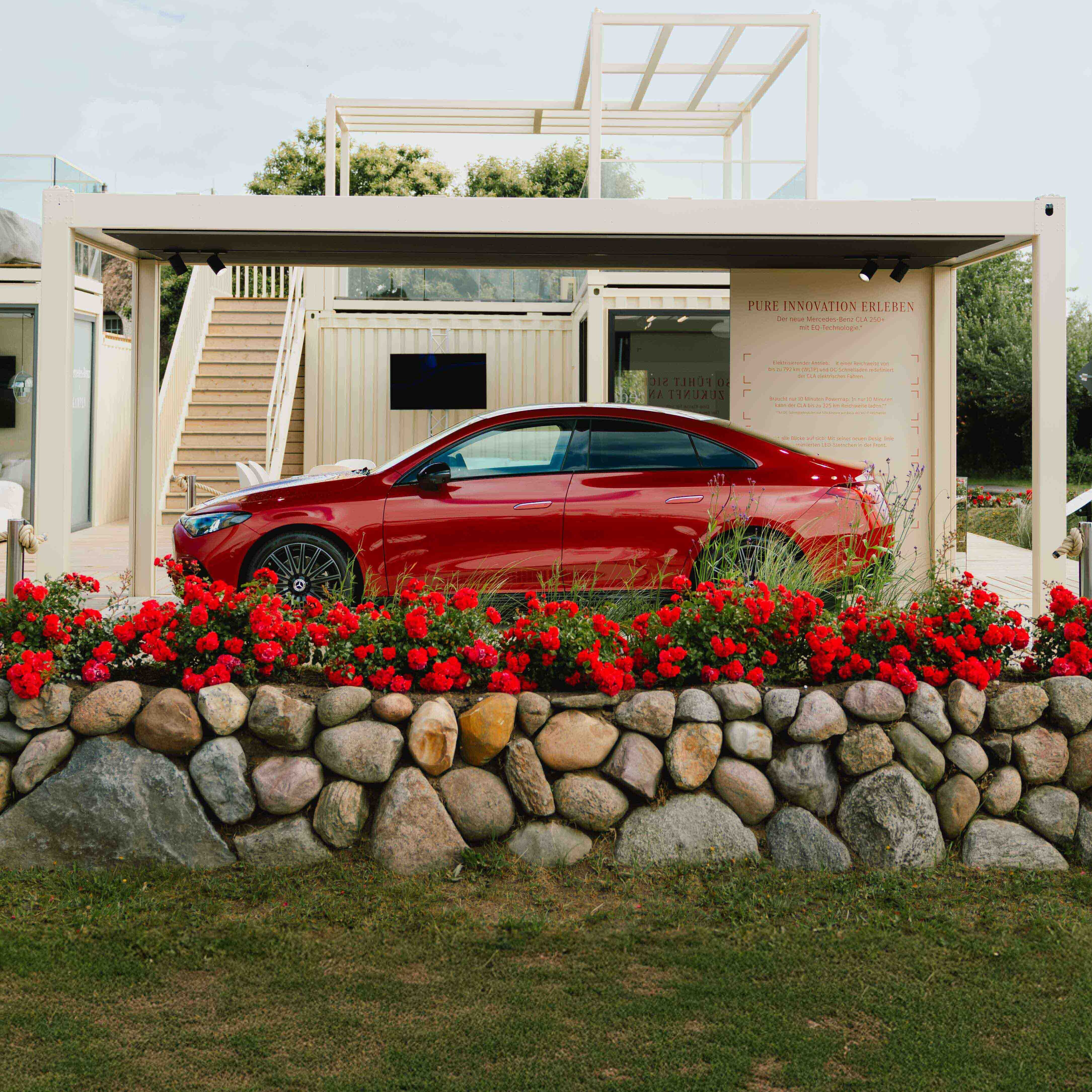 Ein roter CLA hinter einer roten Blumenwand parkend vor einem modernen Gebäude.