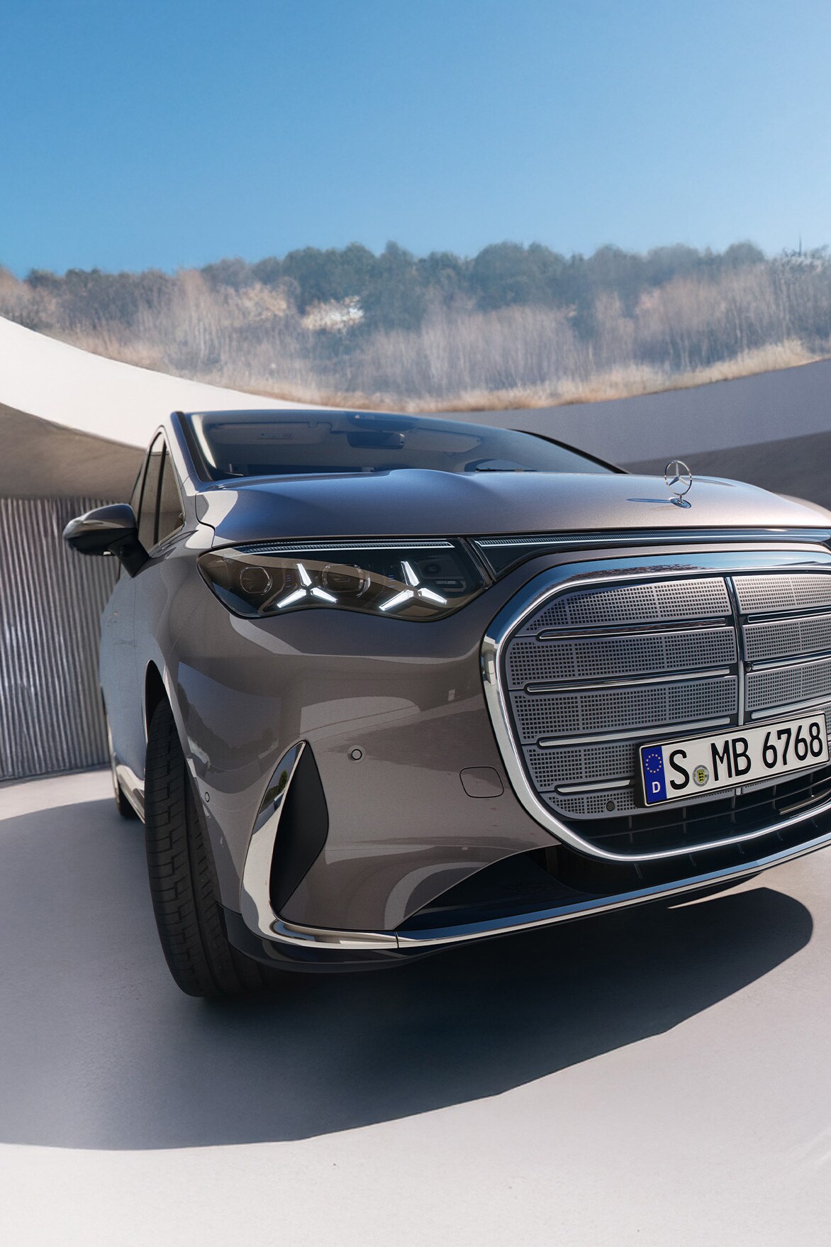 Gezeigt wird der VLE von Mercedes-Benz. Parkend vor einem modernem Gebäude mit einem Kirschbaum an der Seite.