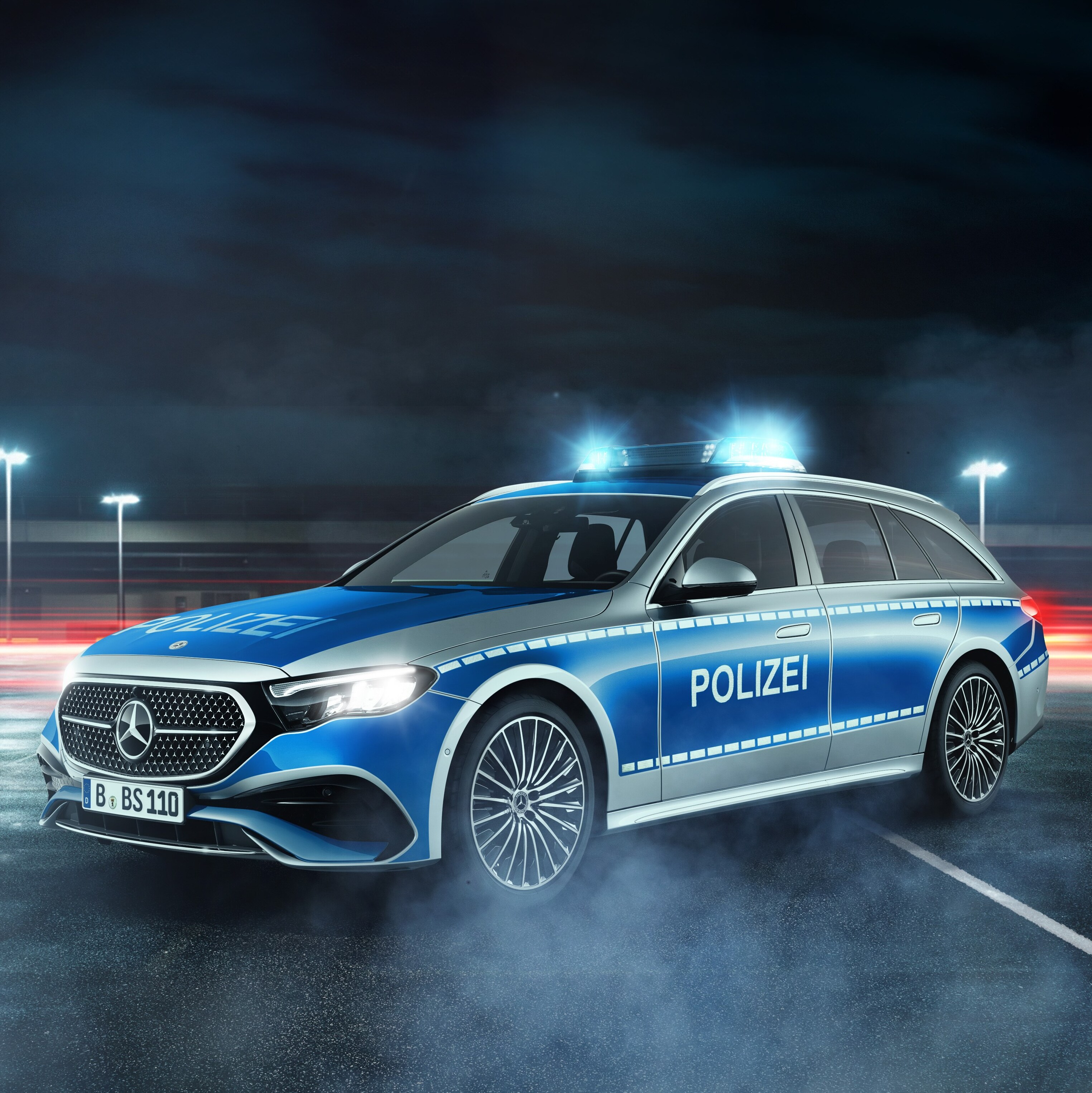 Ein Mercedes-Benz Polizei Fahrzeug bei Nacht mit eingeschaltetem Blaulicht auf einem Parkplatz.
