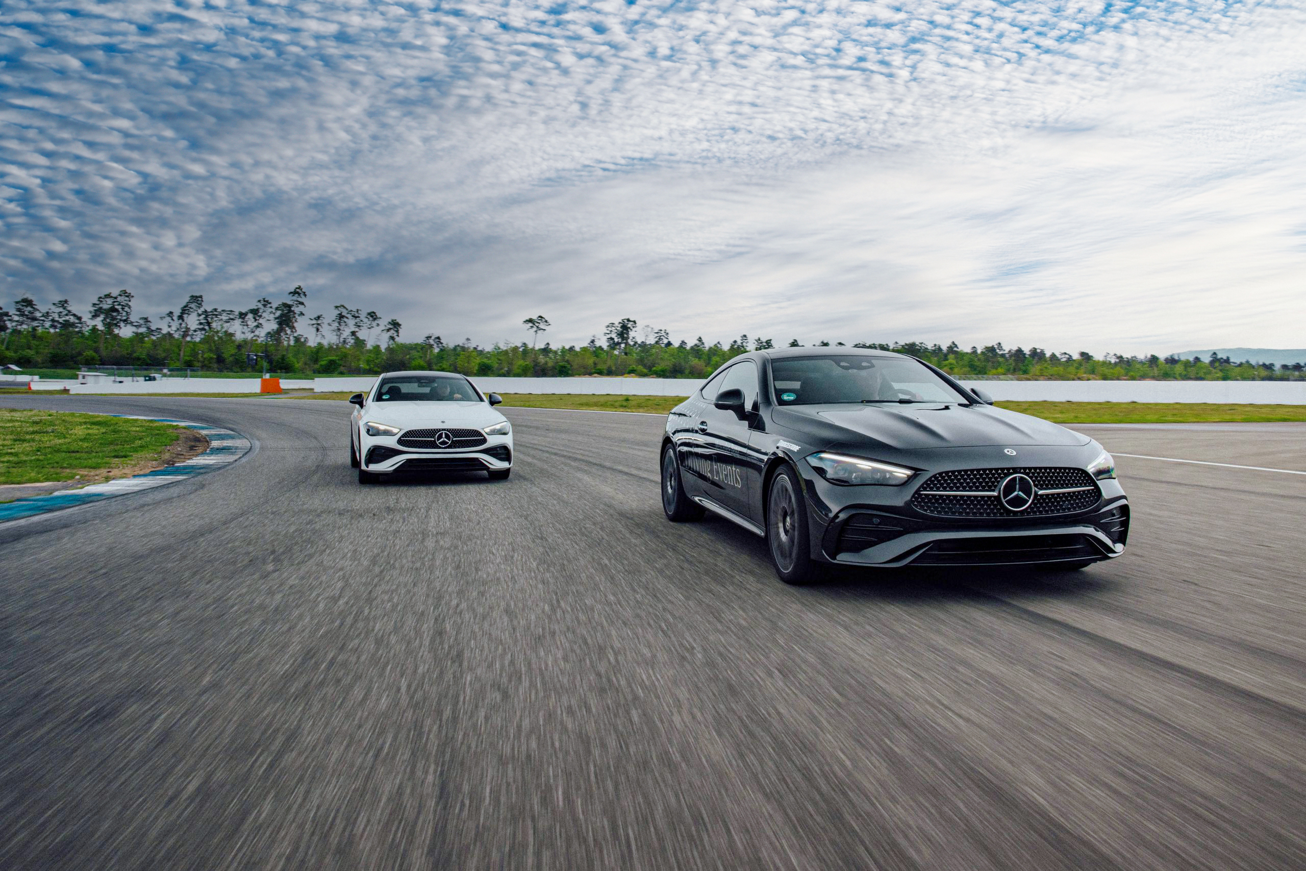 Driving Events | Mercedes-Benz Zwei Fahrzeuge von Mercedes-Benz von vorne auf einer Rennstrecke vor einer weiten Strecke.