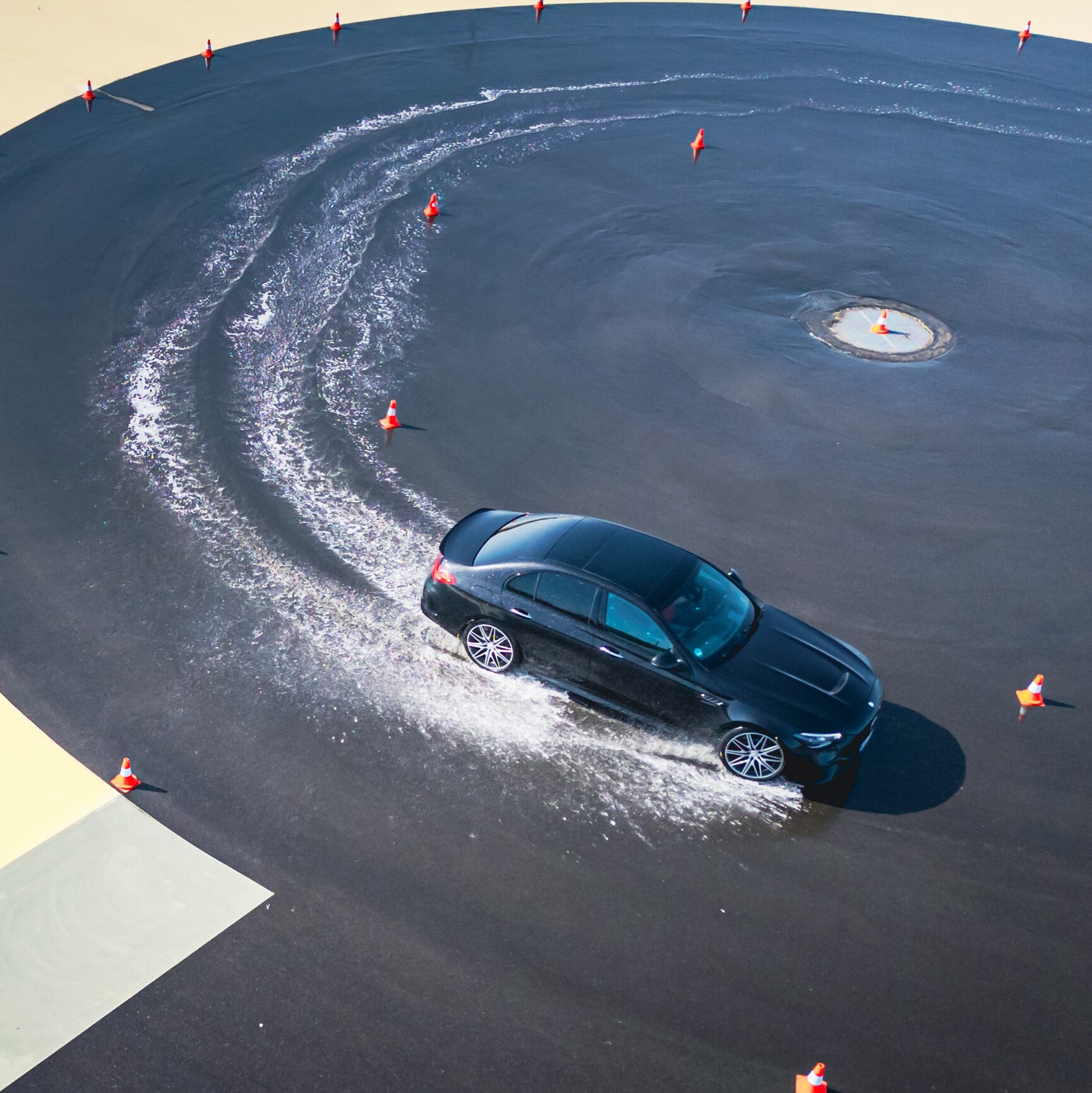 Ein schwarzes Fahrzeug von Mercedes-Benz auf einer nassen Fahrbahn, dass einen Drift fährt.