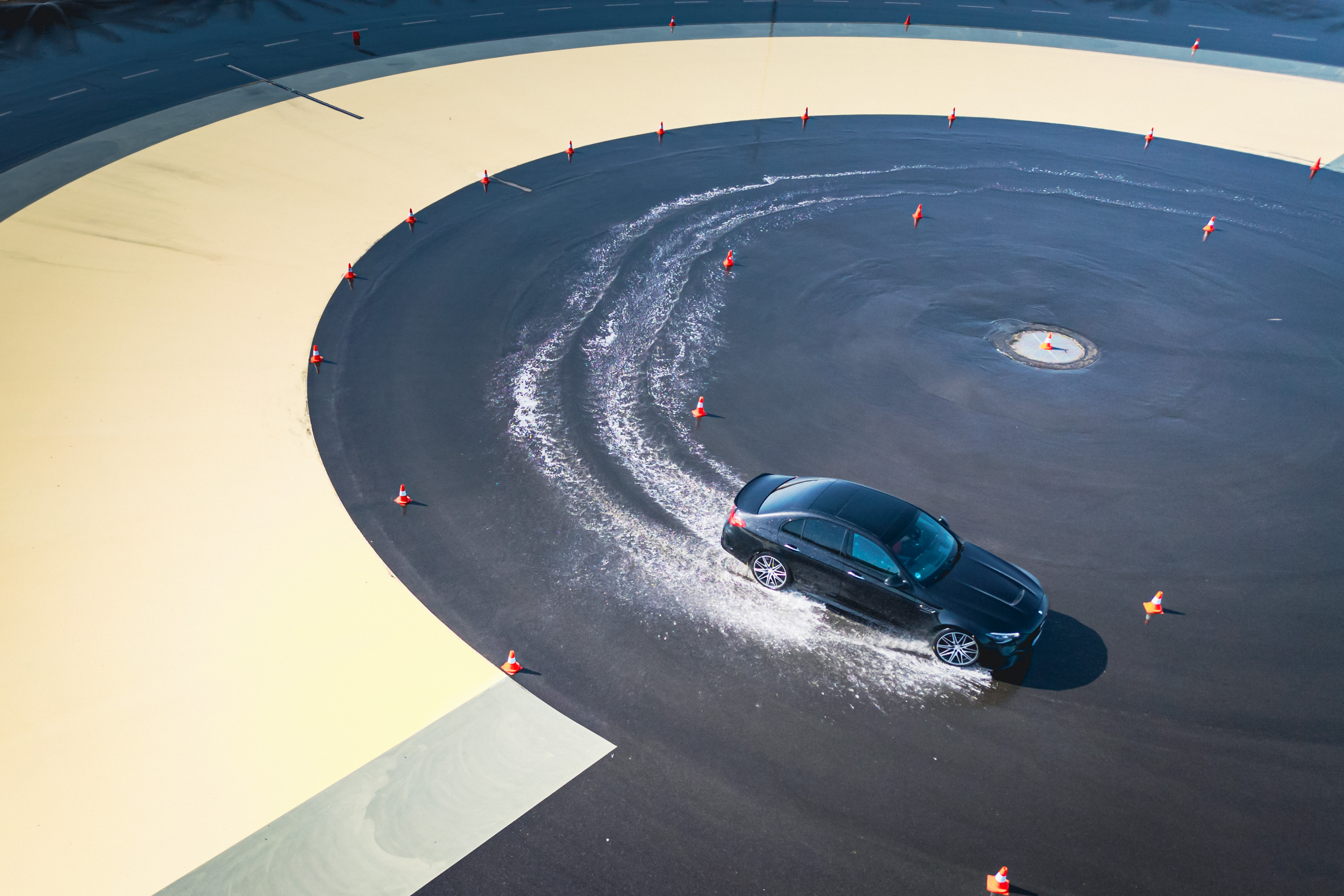 Driving Events | Mercedes-Benz. Ein schwarzes Fahrzeug von Mercedes-Benz auf einer nassen Fahrbahn, dass einen Drift fährt.