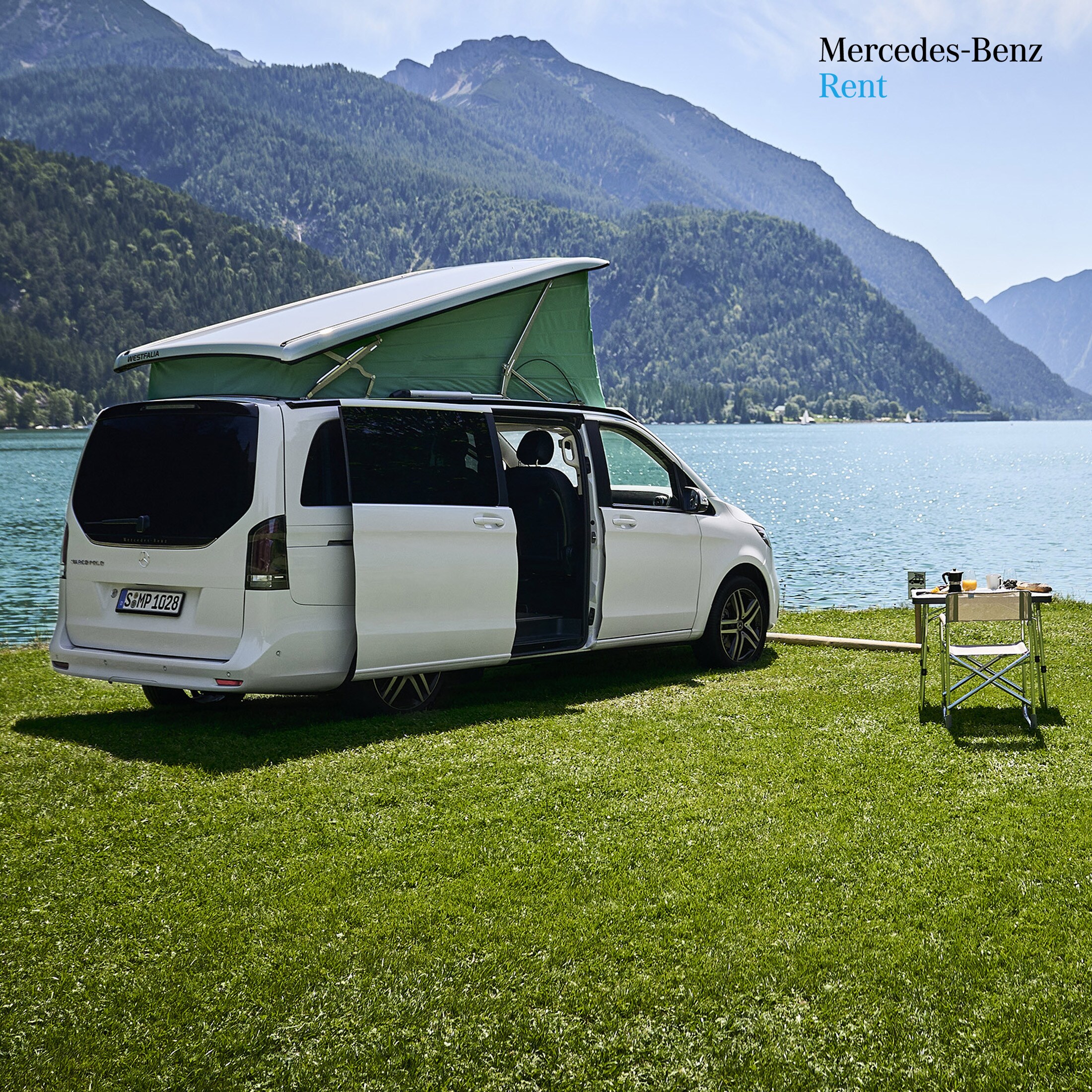 Eine weiße Mercedes-Benz V-Klasse Marco Polo vor einem See mit Bergen im Hintergrund.