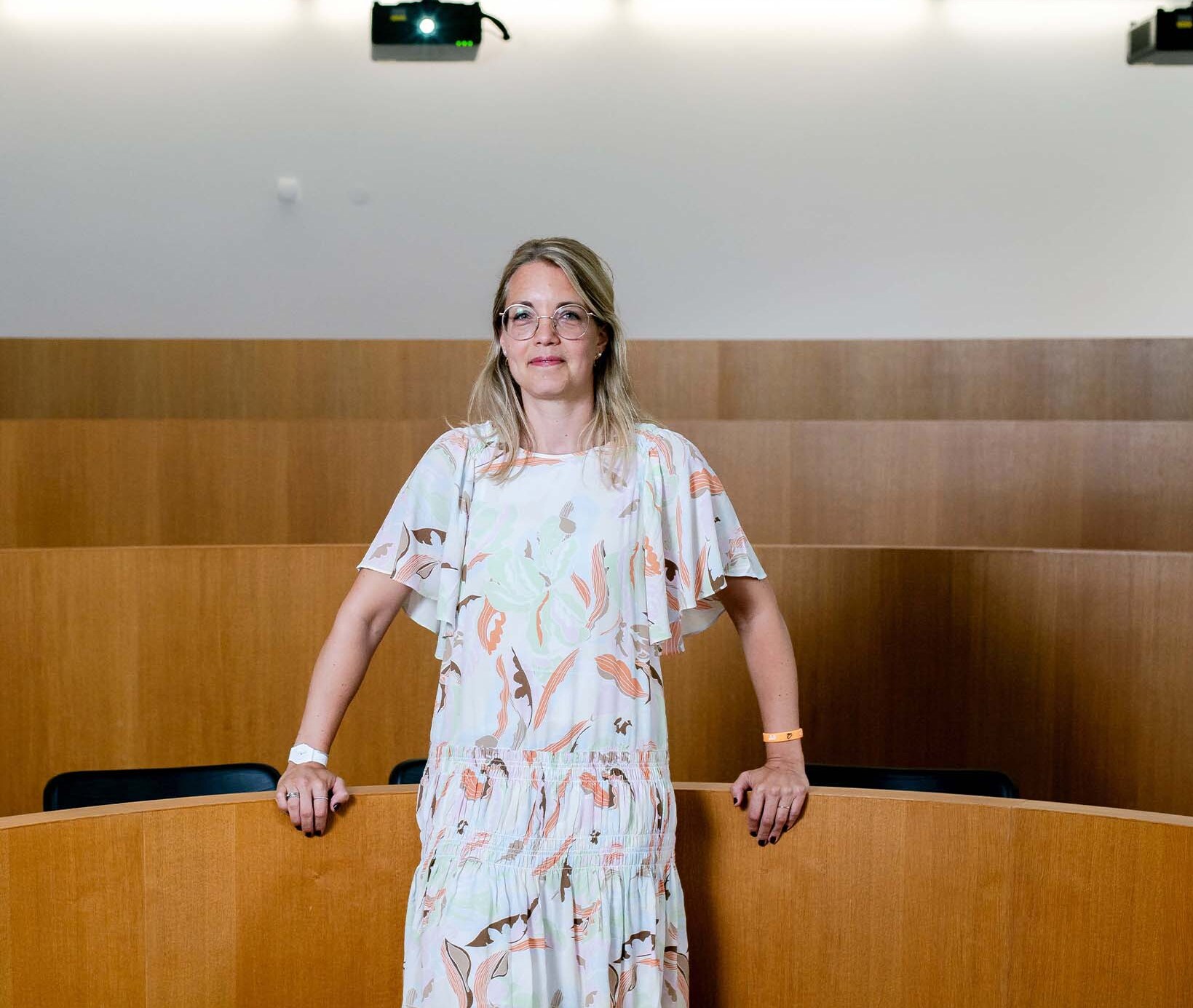 Prof. Dr. Christine Laudenbach steht in einem hellen Kleid in einem leeren Hörsaal.