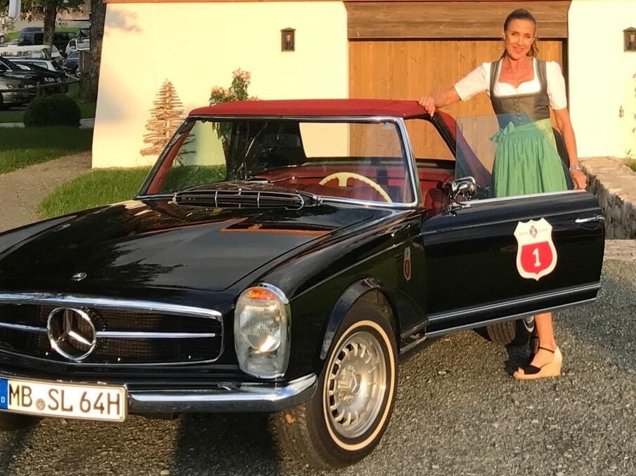 Susanne Gräfin von Moltke steht in einer Tracht neben einem Mercedes-Benz Oldtimer.