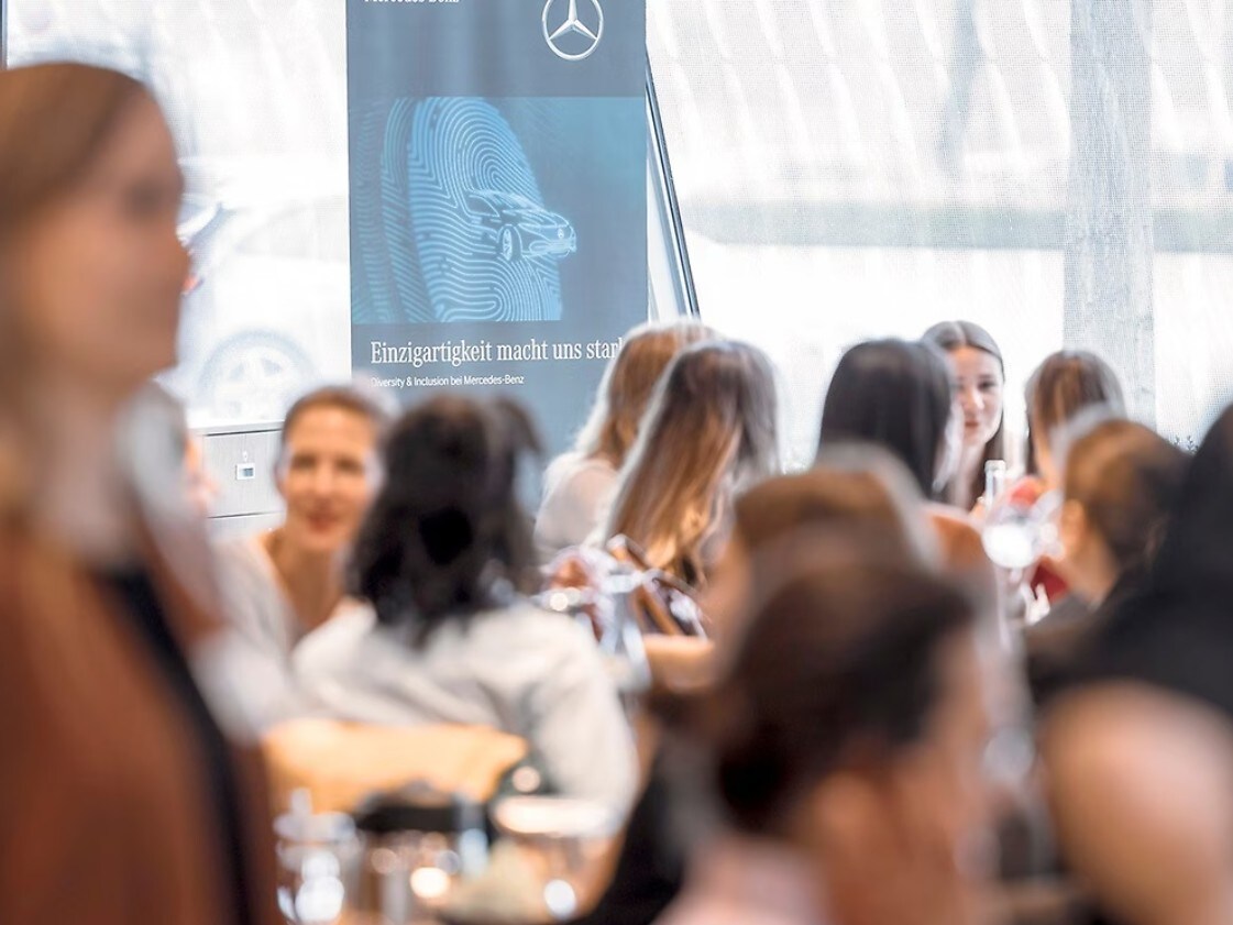 Mehrere Frauen stehen in einem Konferenzraum auf einer Veranstaltung und unterhalten sich angeregt.