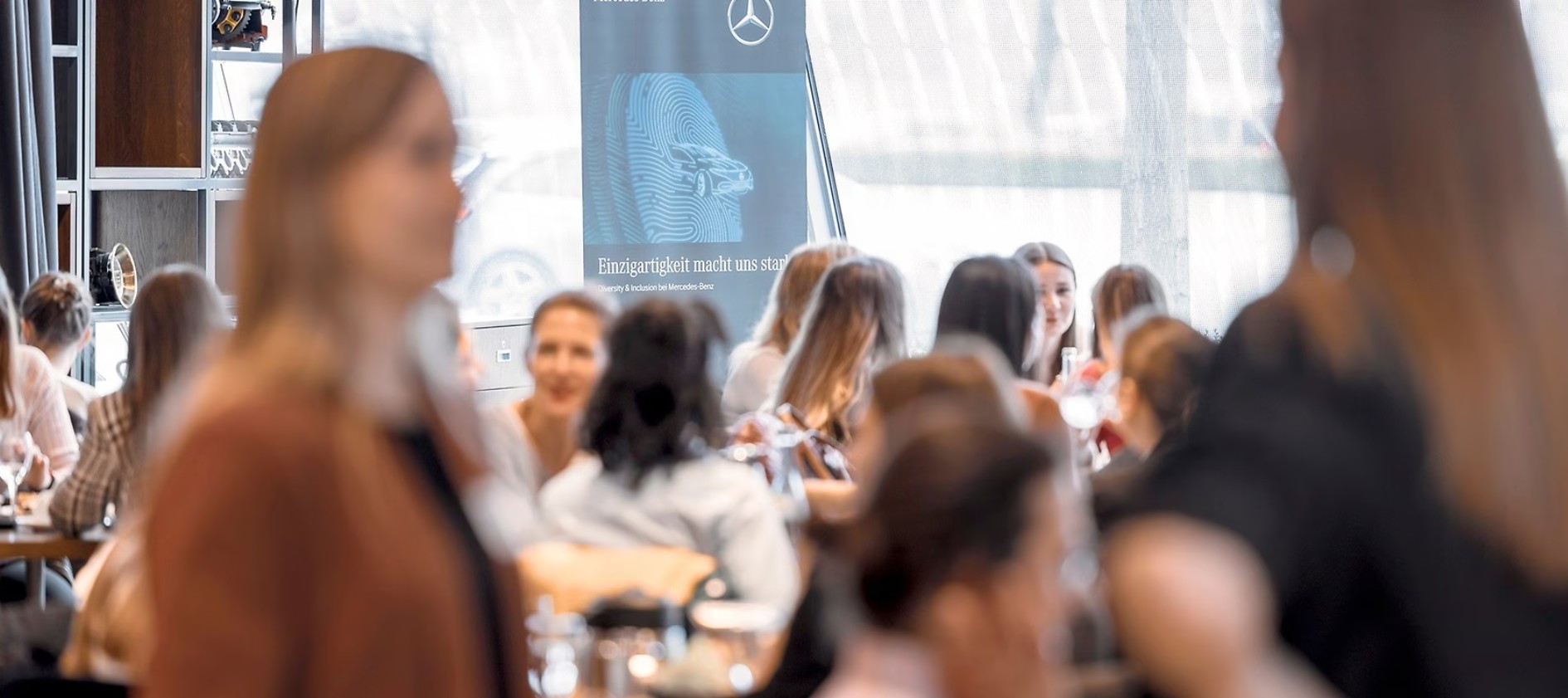 She's Mercedes Empowerment | Mercedes-Benz Mehrere Frauen stehen in einem Konferenzraum auf einer Veranstaltung und unterhalten sich angeregt.