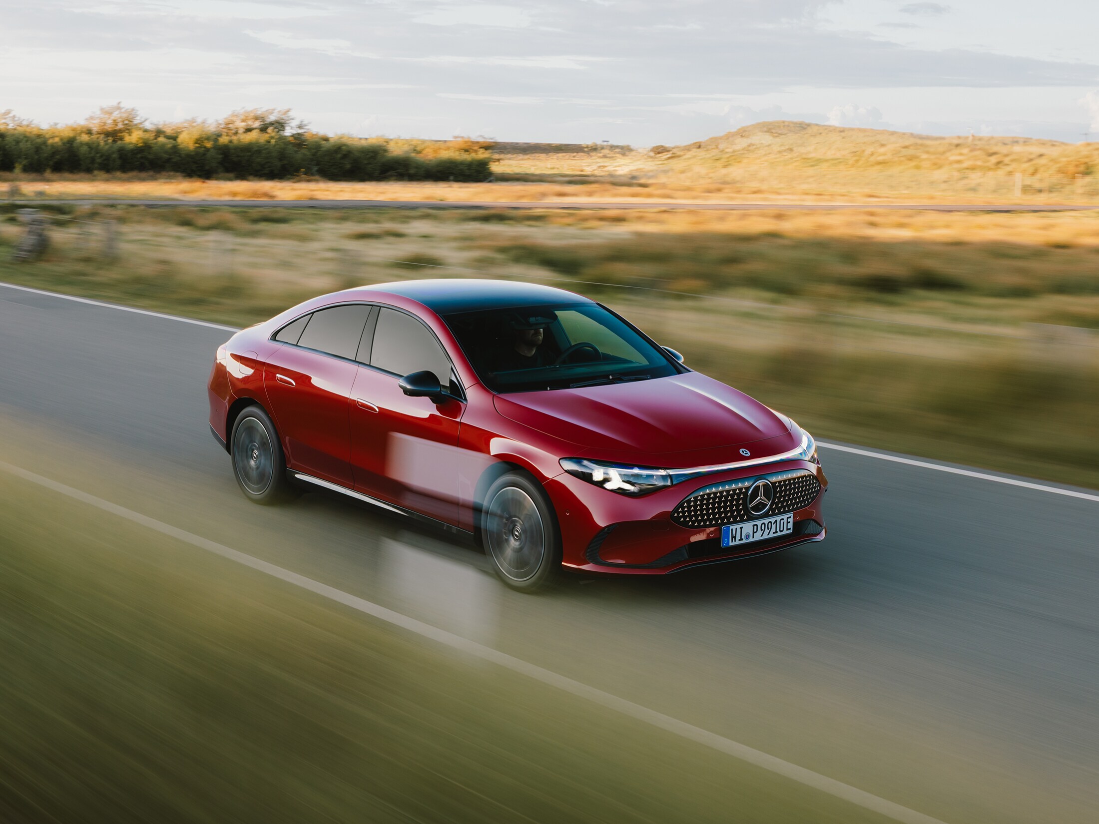 Ein roter elektrischer CLA fährt auf einer Straße zwischen weiten Grasfeldern auf Sylt.