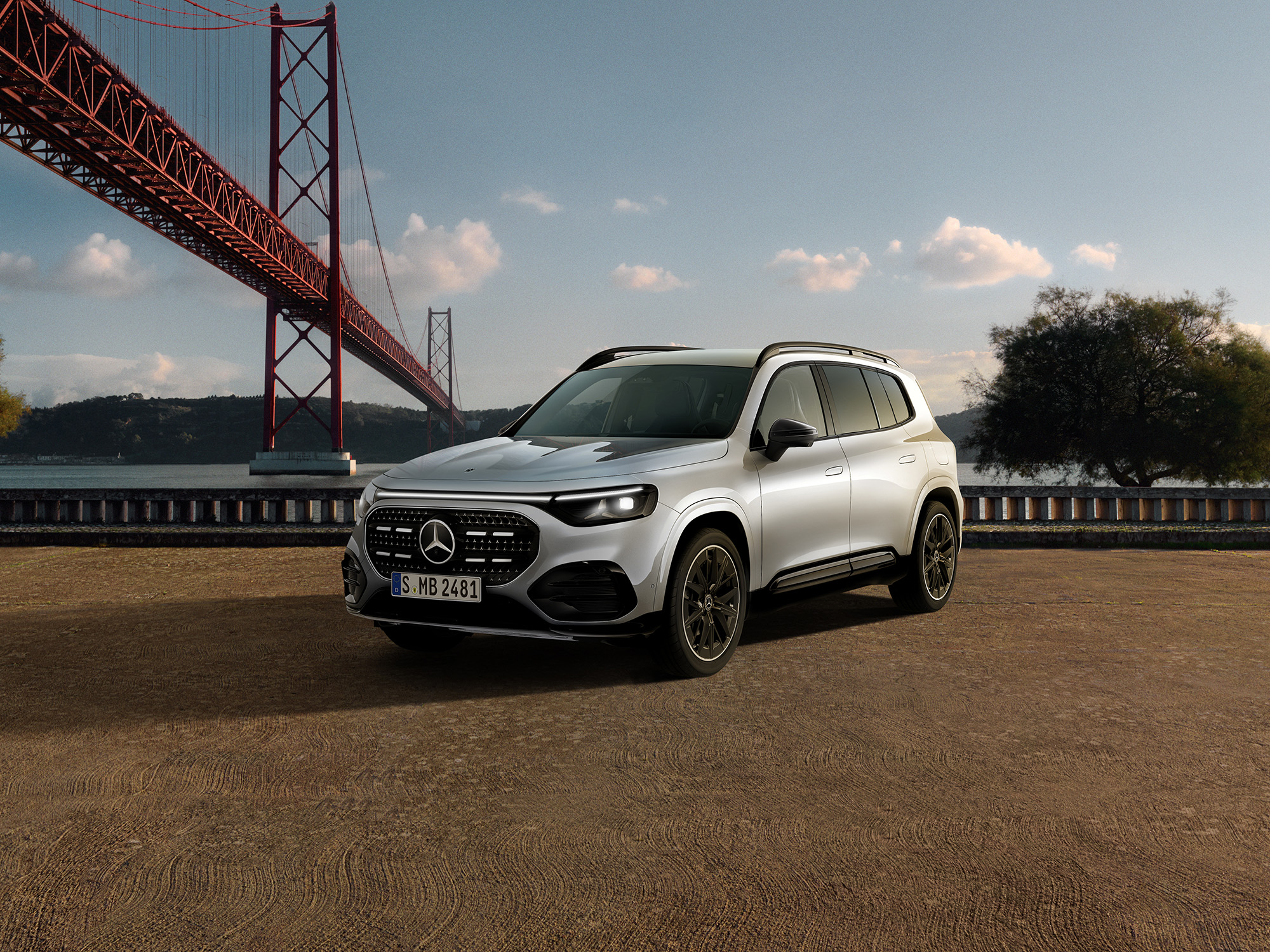 140 Jahre Innovation | Mercedes-Benz Ein silberner Mercedes-Benz GLB in Frontalasicht steht vor einer Brücke am Wasser.