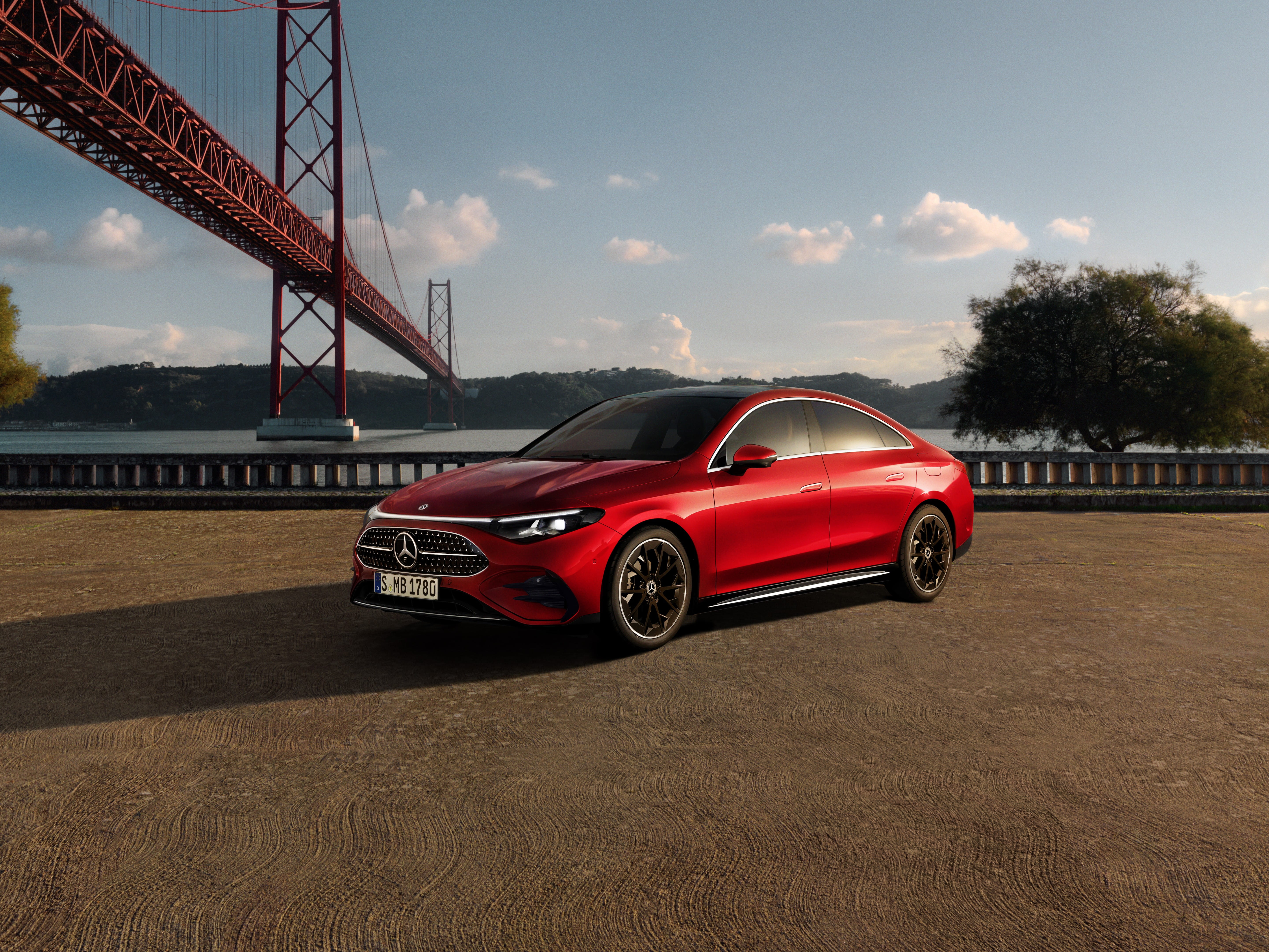 140 Jahre Innovation | Mercedes-Benz Ein roter Mercedes-Benz CLA in Frontalasicht steht vor einer Brücke am Wasser im Sonnenuntergang.