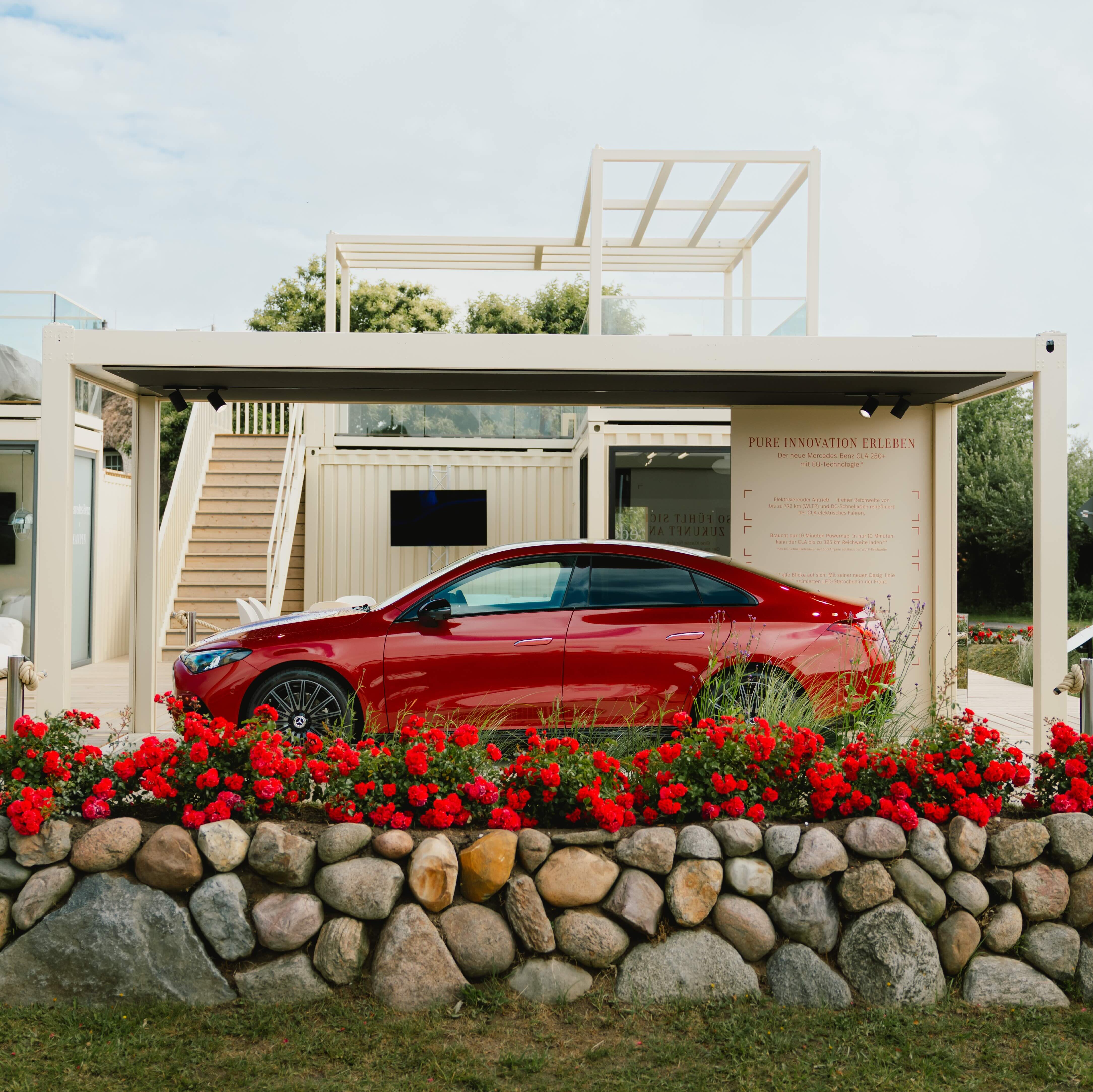 Ein roter CLA hinter einer roten Blumenwand parkend vor einem modernen Gebäude.
