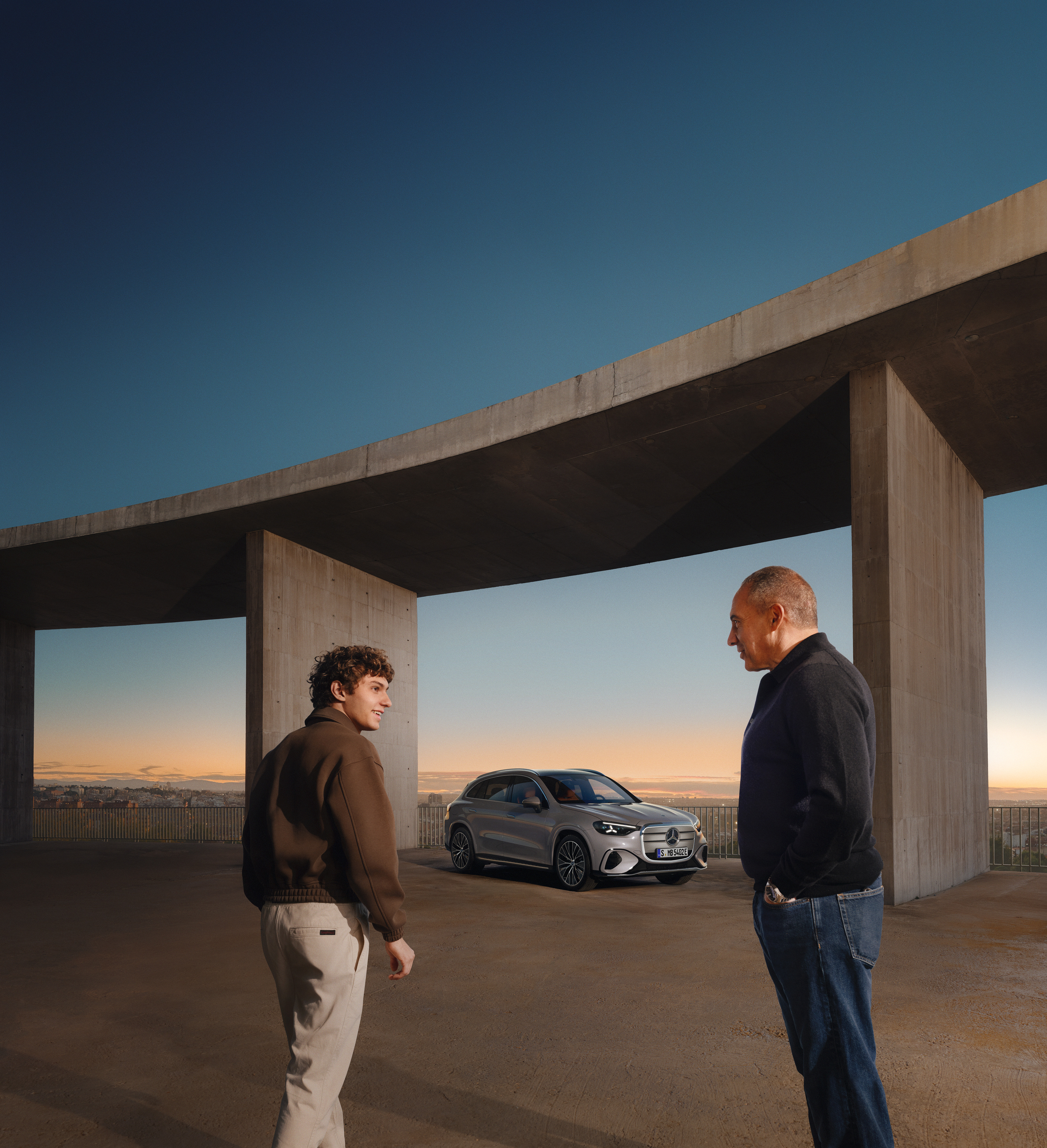 GLC | Mercedes-Benz Kimi Antonelli und sein Vater Marco Antonelli stehen vor einer großen Brücke. Unter der Brücke steht der elektrische GLC.