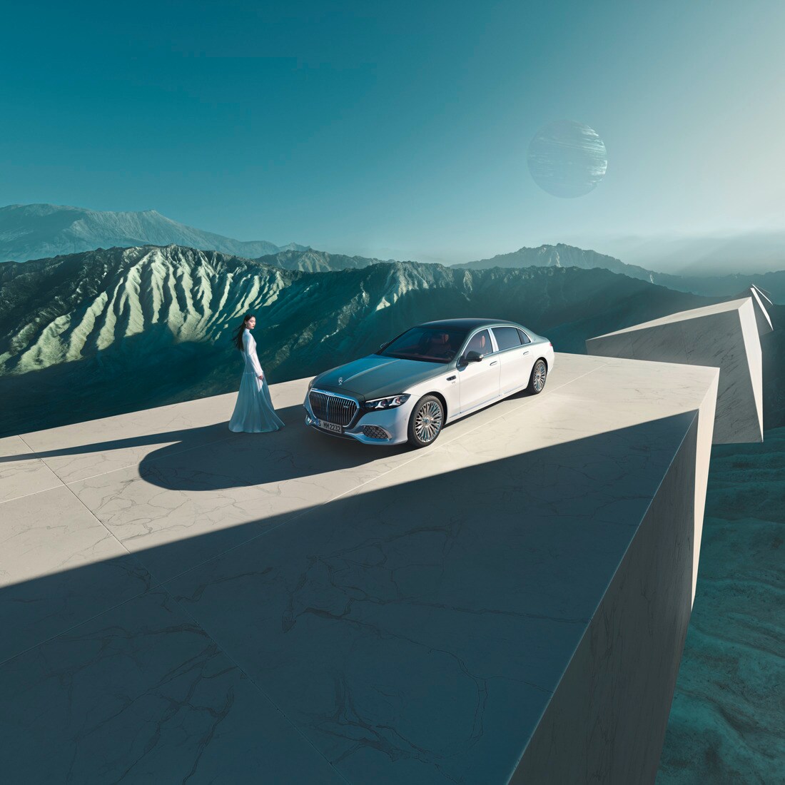 Eine Frau steht neben einer parkenden Mercedes-Maybach S-Klasse. Im Hintergrund eine Bergkulisse.