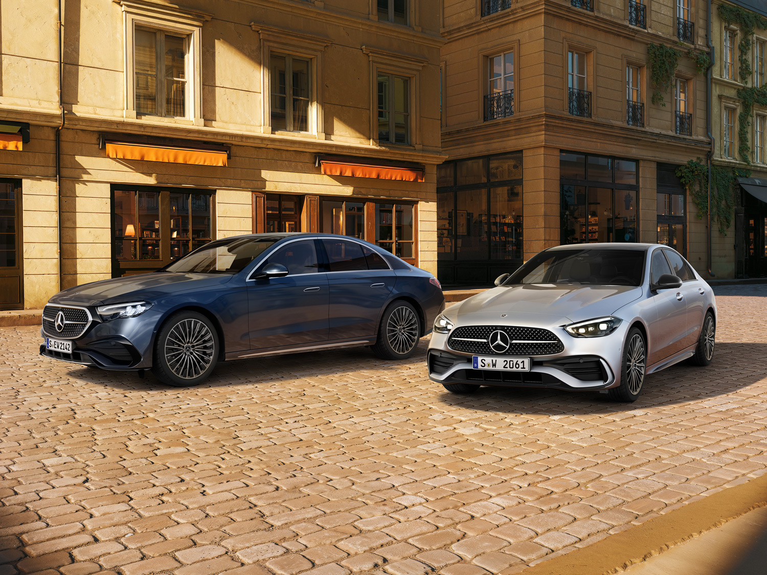 Zeit, die sich lohnt | Mercedes-Benz. Eine C-Klasse und eine E-Klasse stehen auf einer gepflasterten Straße vor gelben Gebäuden.