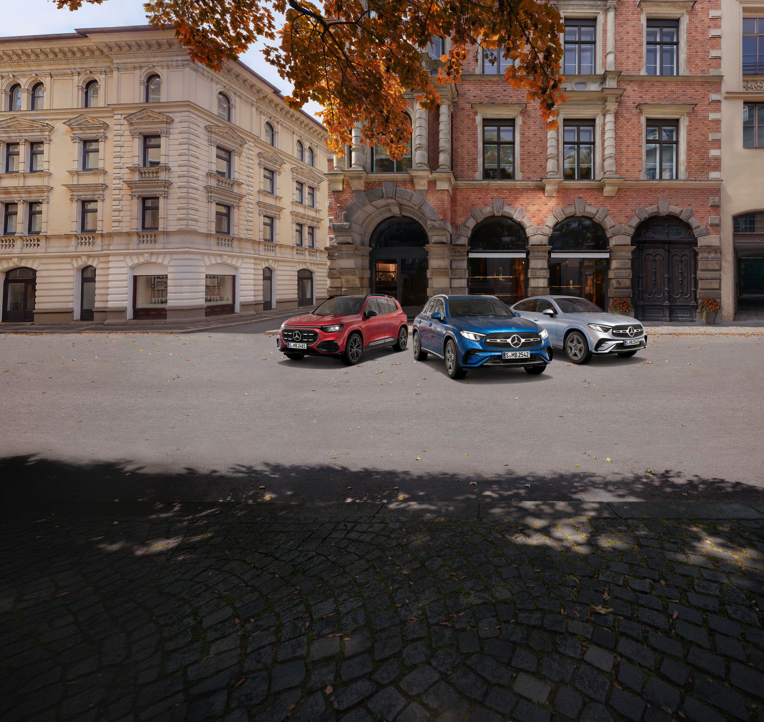 Warum entscheiden | Mercedes-Benz 3 Mercedes-Benz Modelle in Rot, Blau und Silber stehen nebeneinander auf einer Straße in einer urbanen Umgebung. Die Sonne scheint.