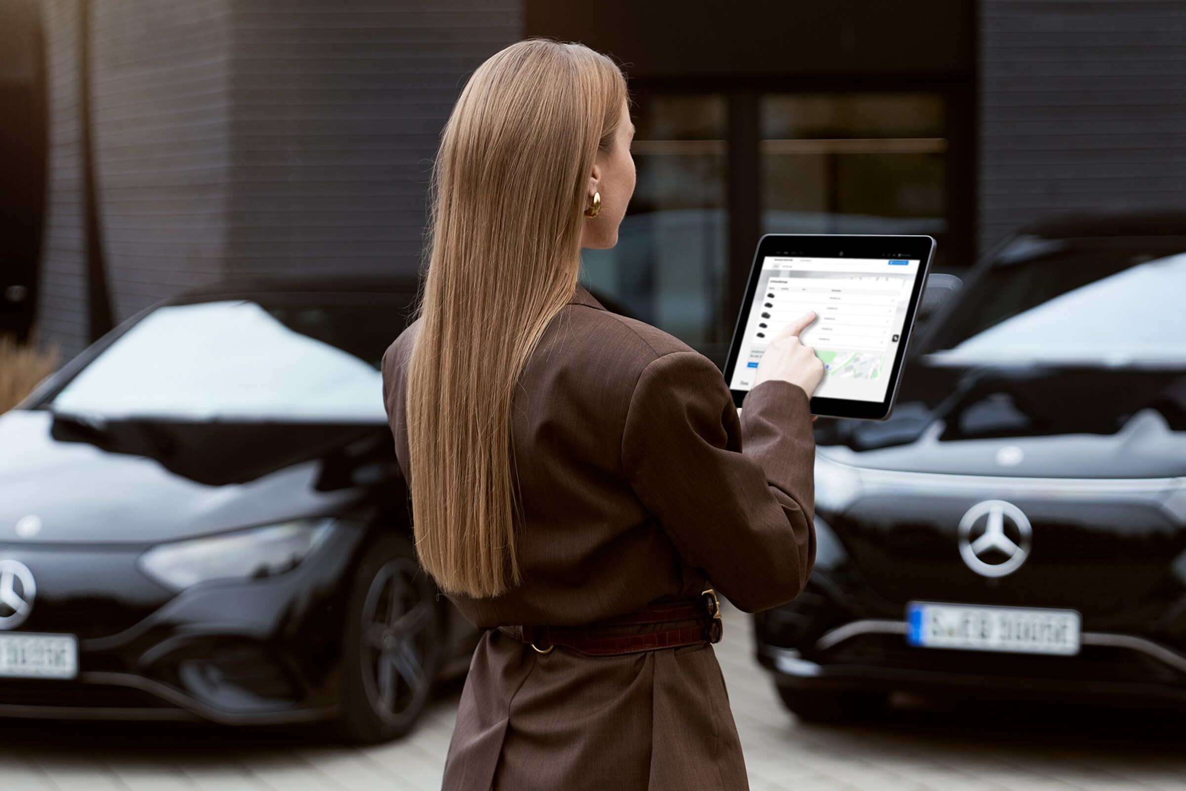 Eine Frau steht mit einem Tablet vor zwei schwarzen Fahrzeugen von Mercedes-Benz.