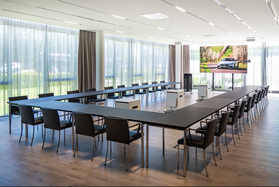 Konferenzen im Kundencenter | Mercedes‑Benz. Ein lichtdurchfluteter Konferenzraum mit u-förmig angeordnetem Tisch und Stühlen drumherum.