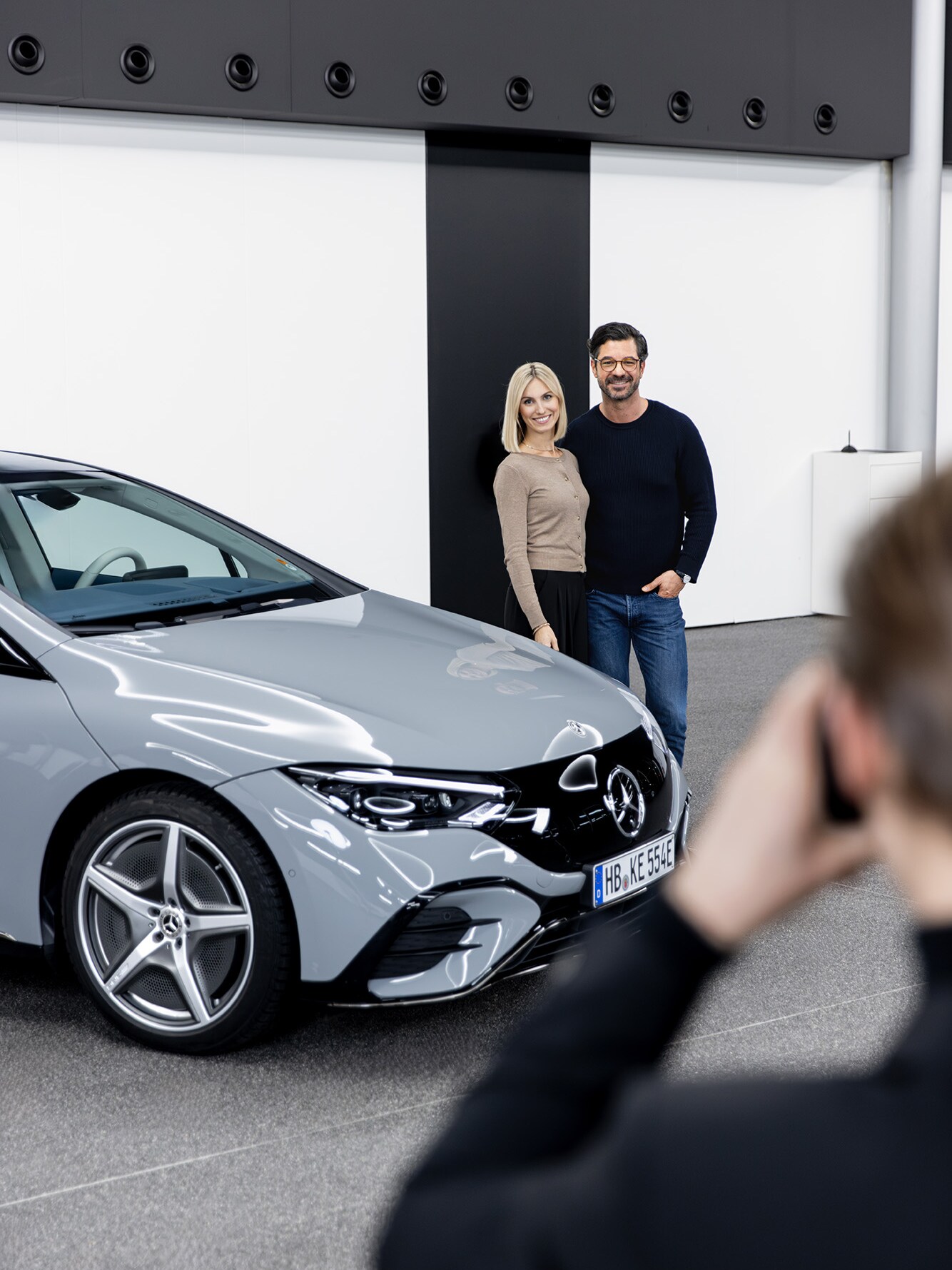 Ein Paar steht hinter einem hellen Mercedes-Benz Modell und wird dabei fotografiert.