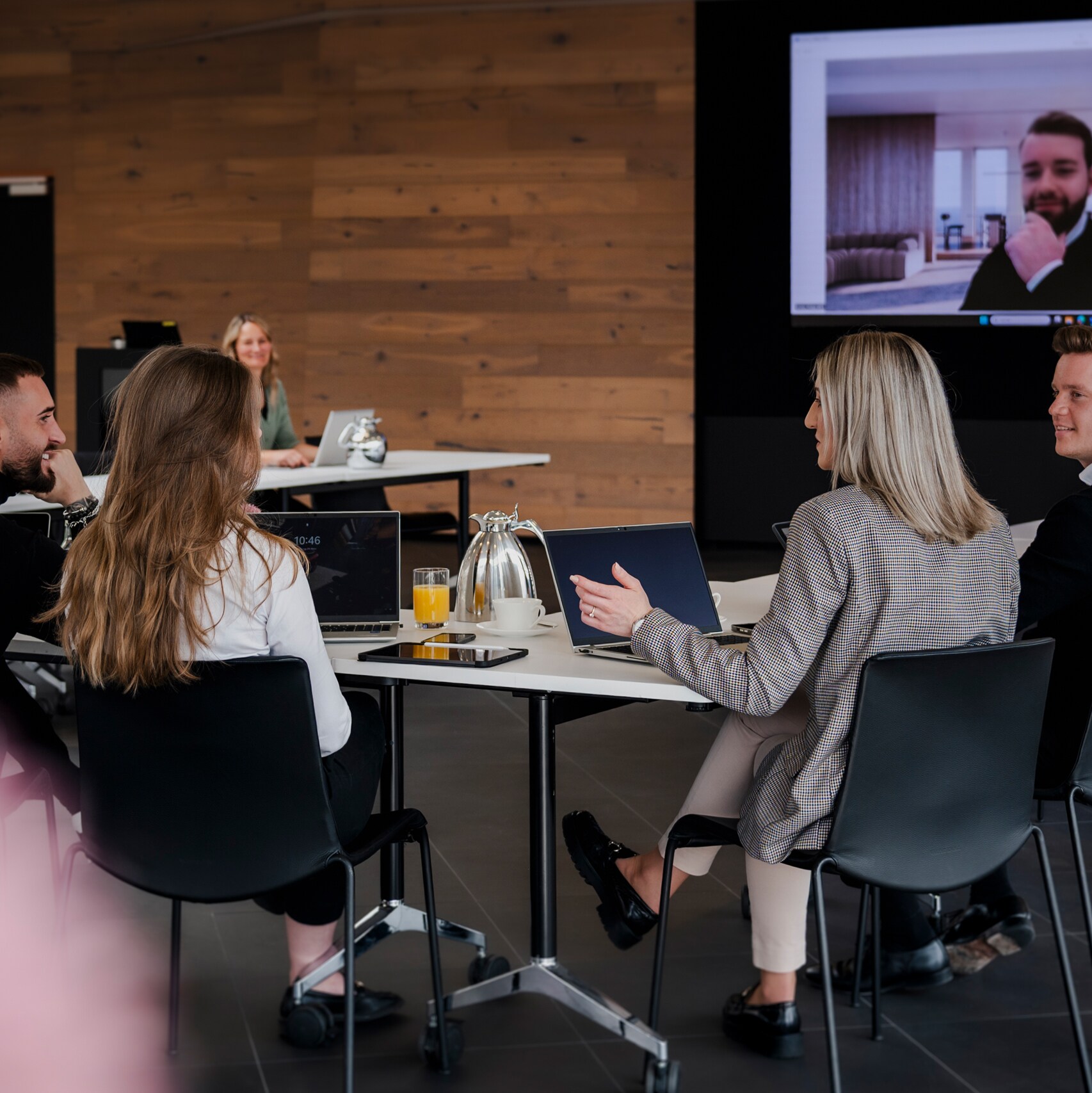 Fünf Personen sitzen an einem Konferenztisch und schauen auf einen Videoleinwand mit einem weiteren Gesprächsteilnehmer.