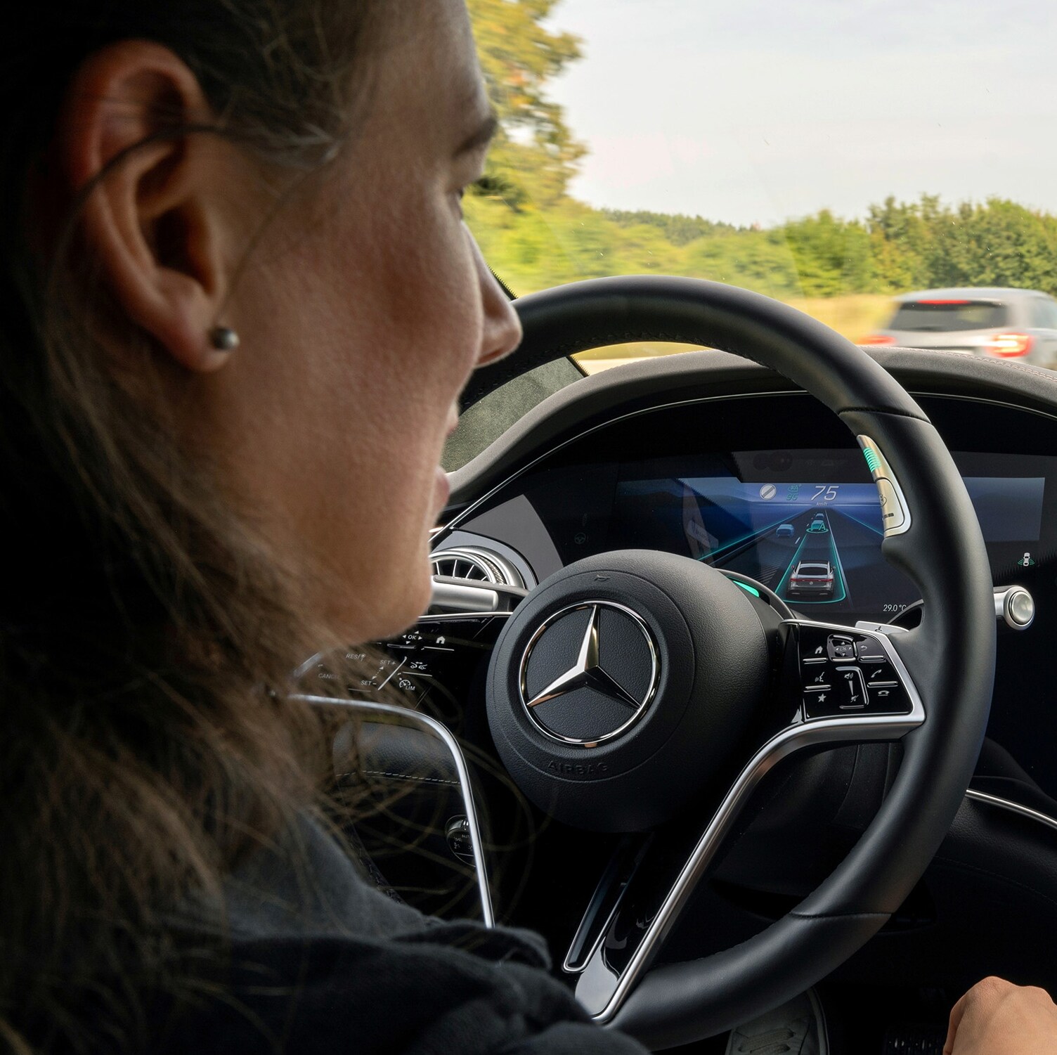 Eine Frau sitzt am Steuer eines Fahrzeugs von Mercedes-Benz und testet neue Funktionen.