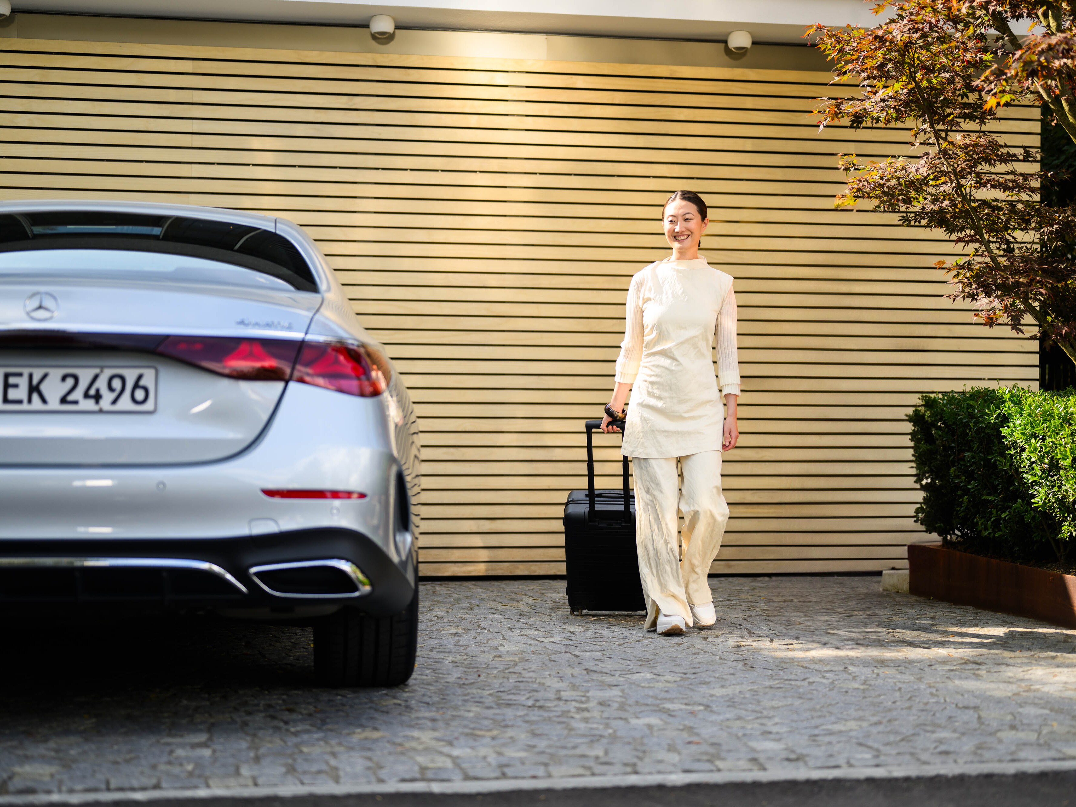 Eine Person mit Rollkoffer läuft neben einem Mercedes-Benz Fahrzeug.