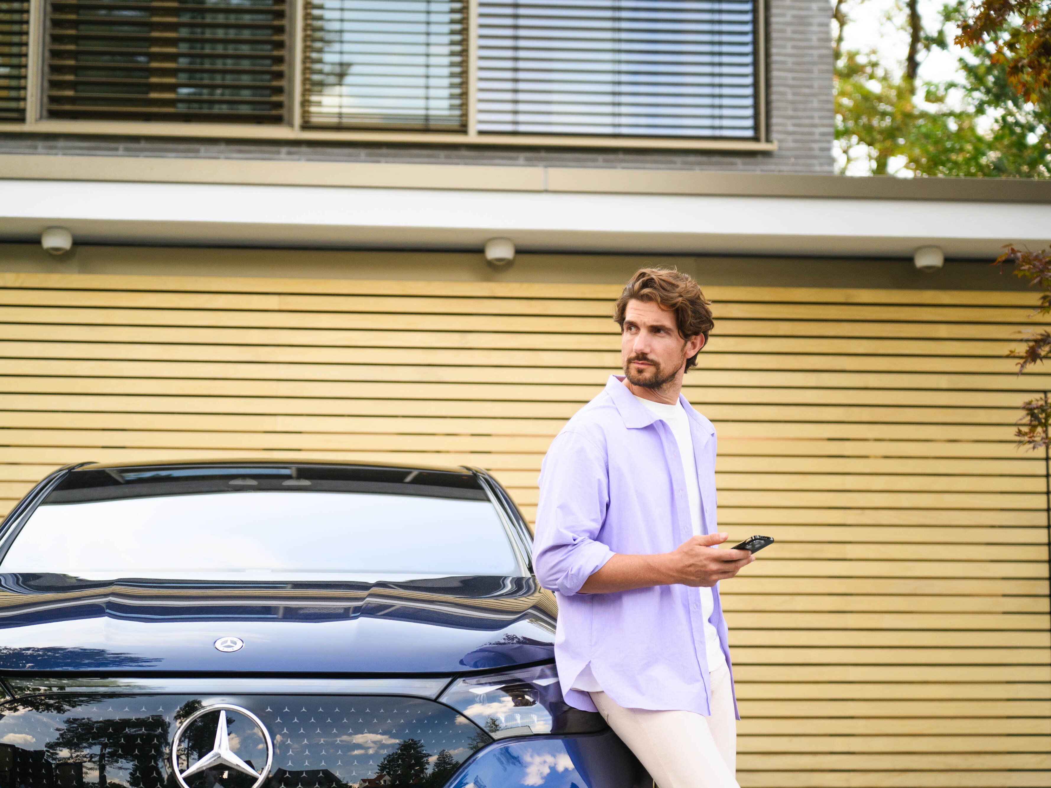 Eine Person mit Smartphone steht vor einem geparkten Mercedes-Benz.