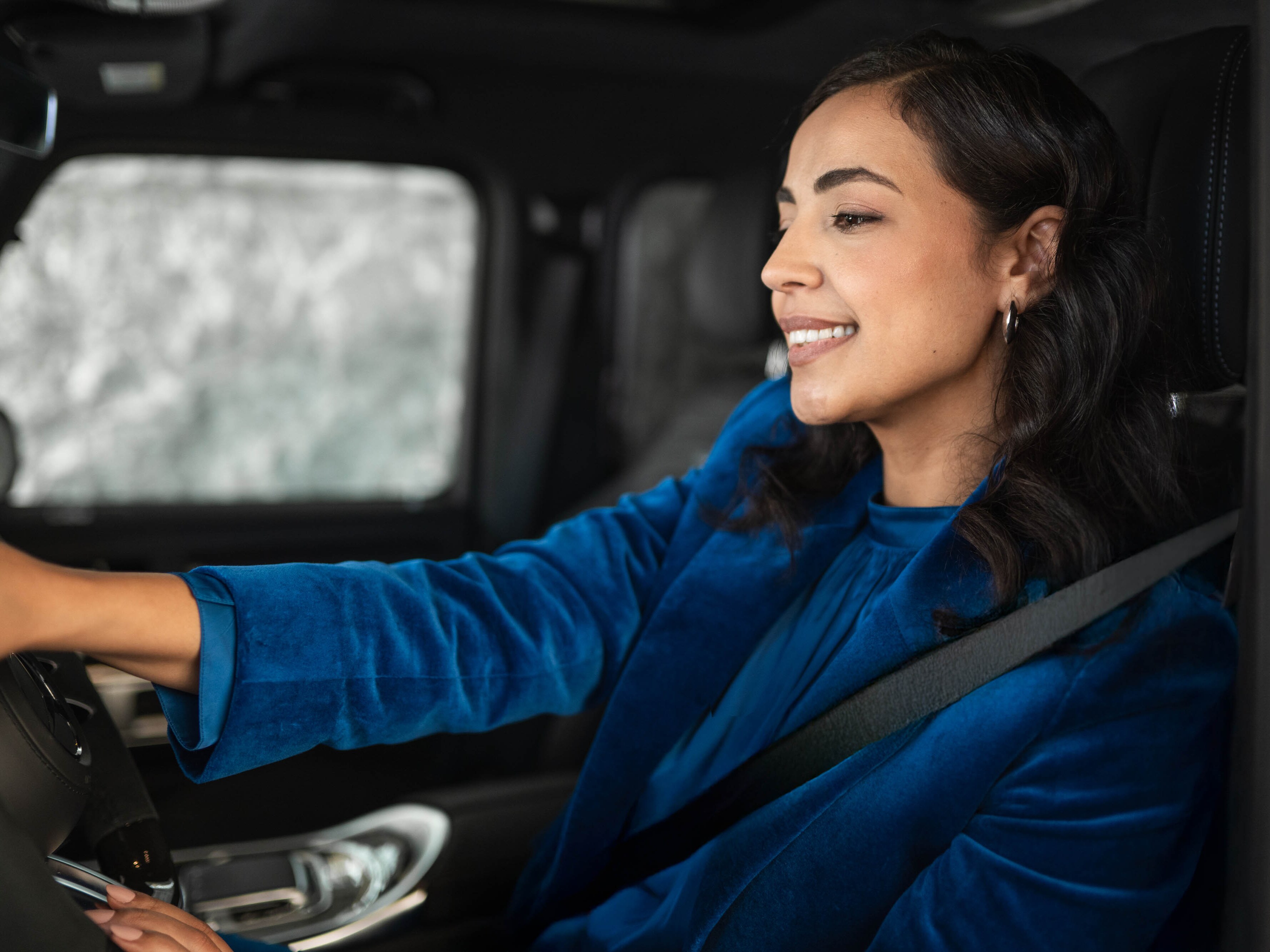 Eine Person mit blauem Mantel lächelt beim Autofahren.