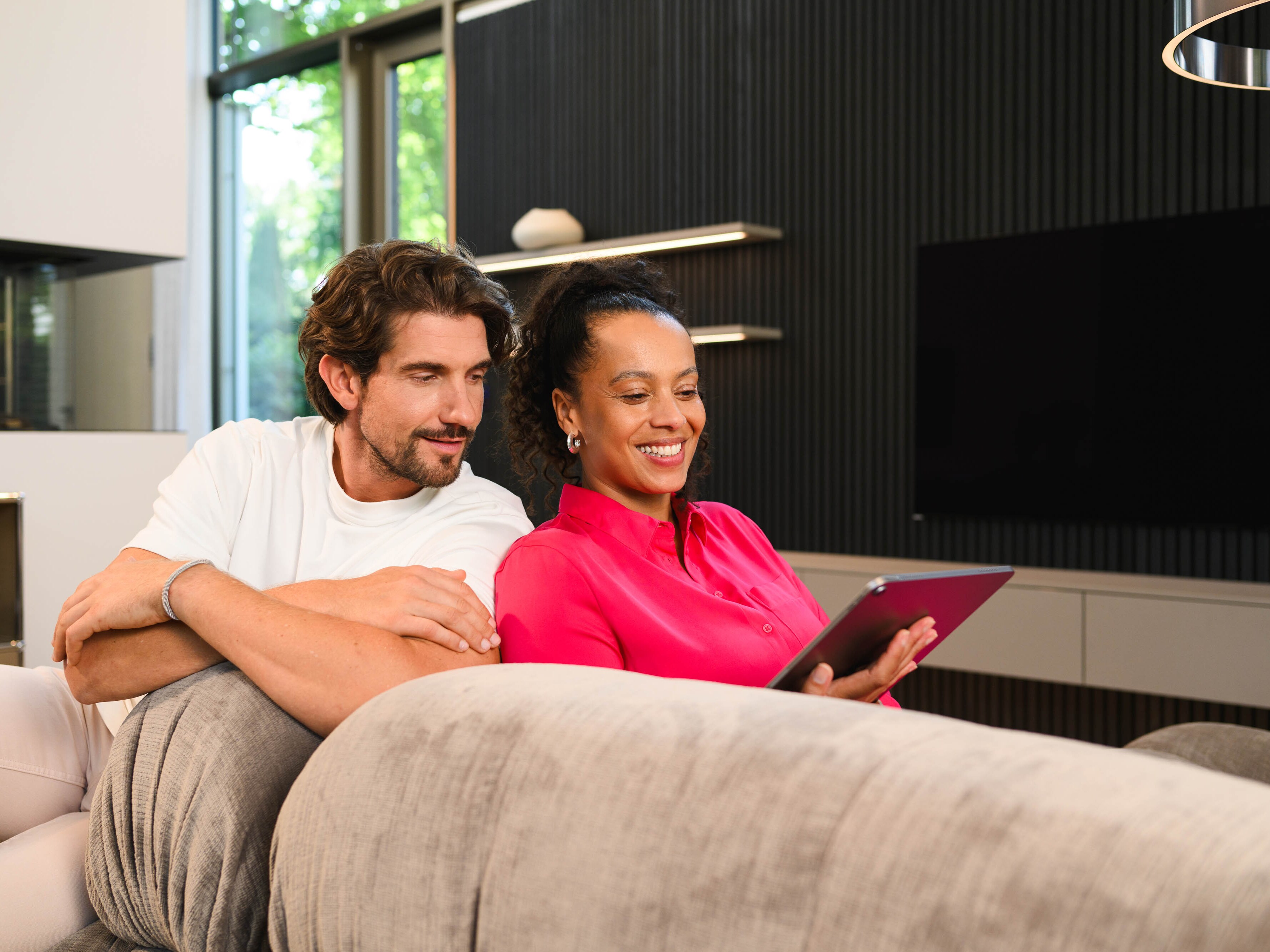 Zwei Menschen auf der Couch schauen auf ein Tablet. 