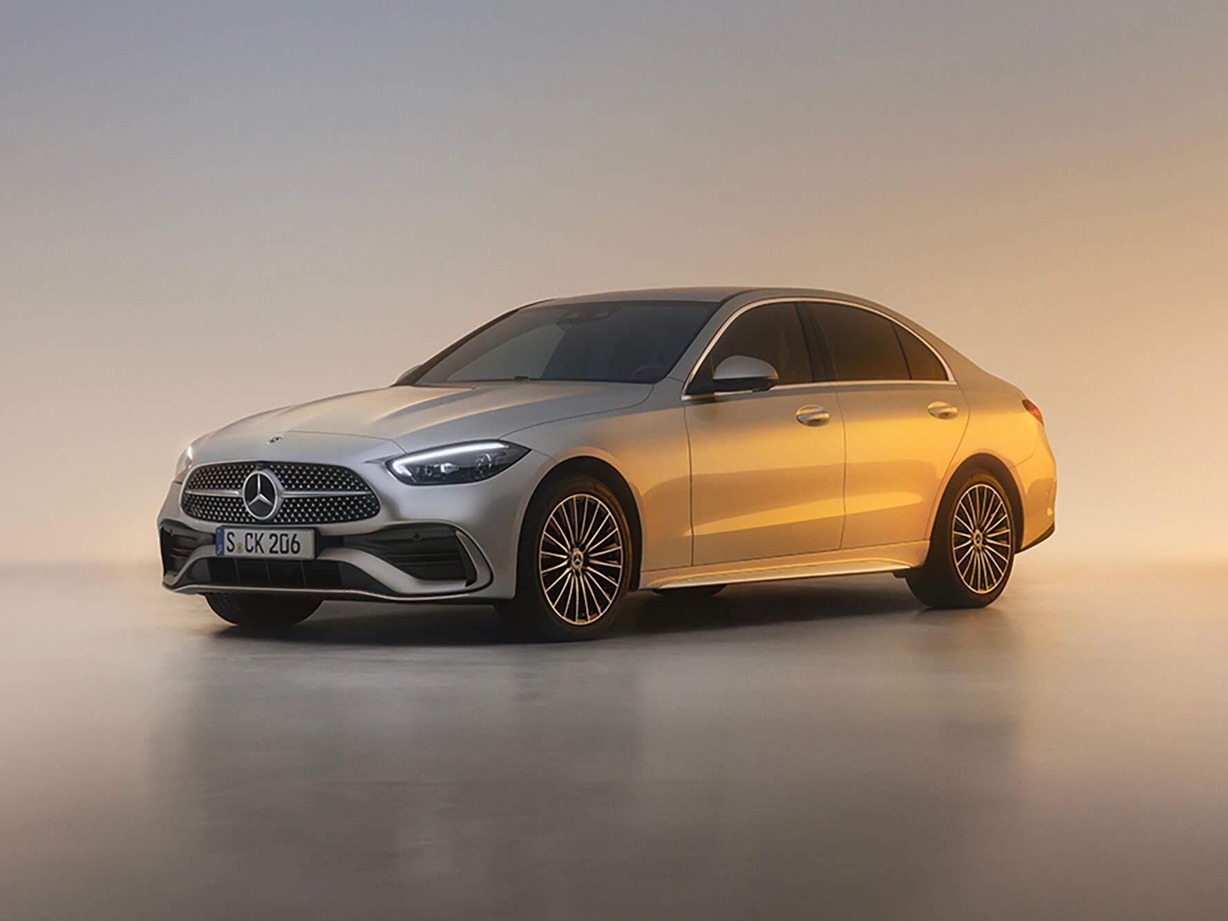 Die C-Klasse Limousine, seitliche Frontansicht. Parkend vor einem hellen Hintergrund im Sonnenuntergang.