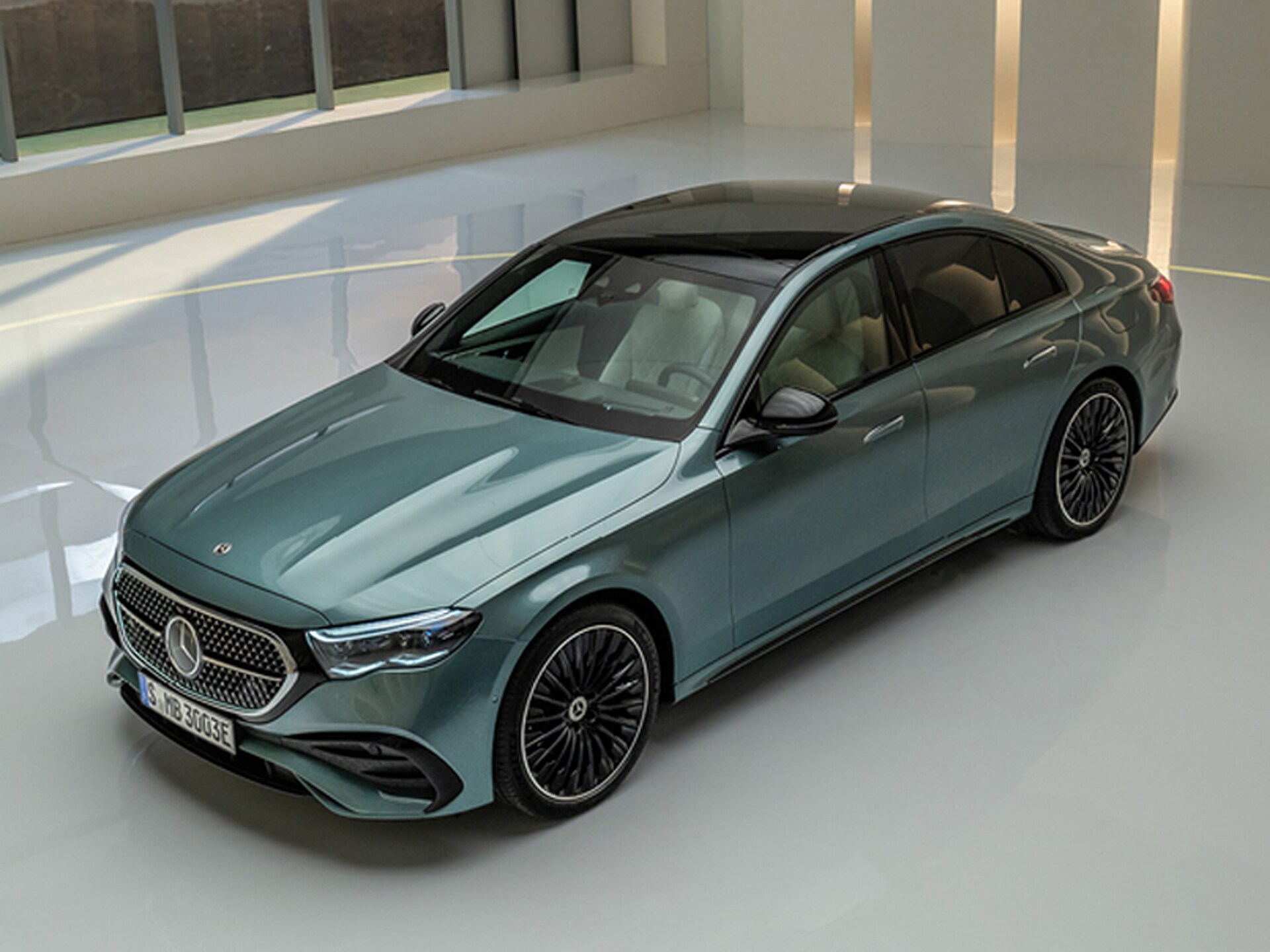 Eine grüne Mercedes-Benz E-Klasse Limousine steht in einem hell beleuchteten, weißen Raum.