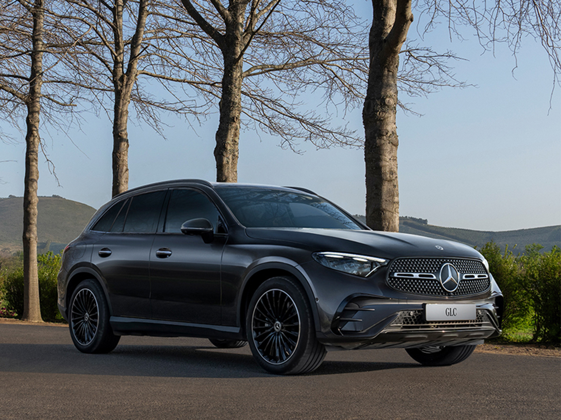 Fahrzeug-Angebote | Mercedes-Benz. Ein schwarzer Mercedes-Benz GLC SUV fährt über eine Landstrasse mit Bergen im Hintergrund.