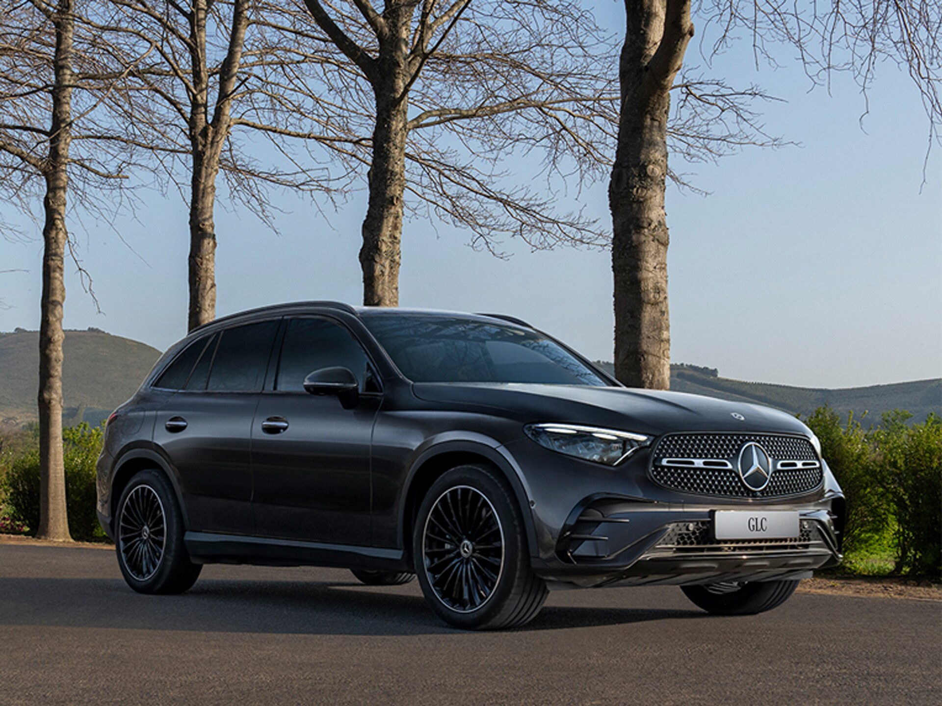 Ein schwarzer Mercedes-Benz GLC SUV fährt über eine Landstrasse mit Bergen im Hintergrund.