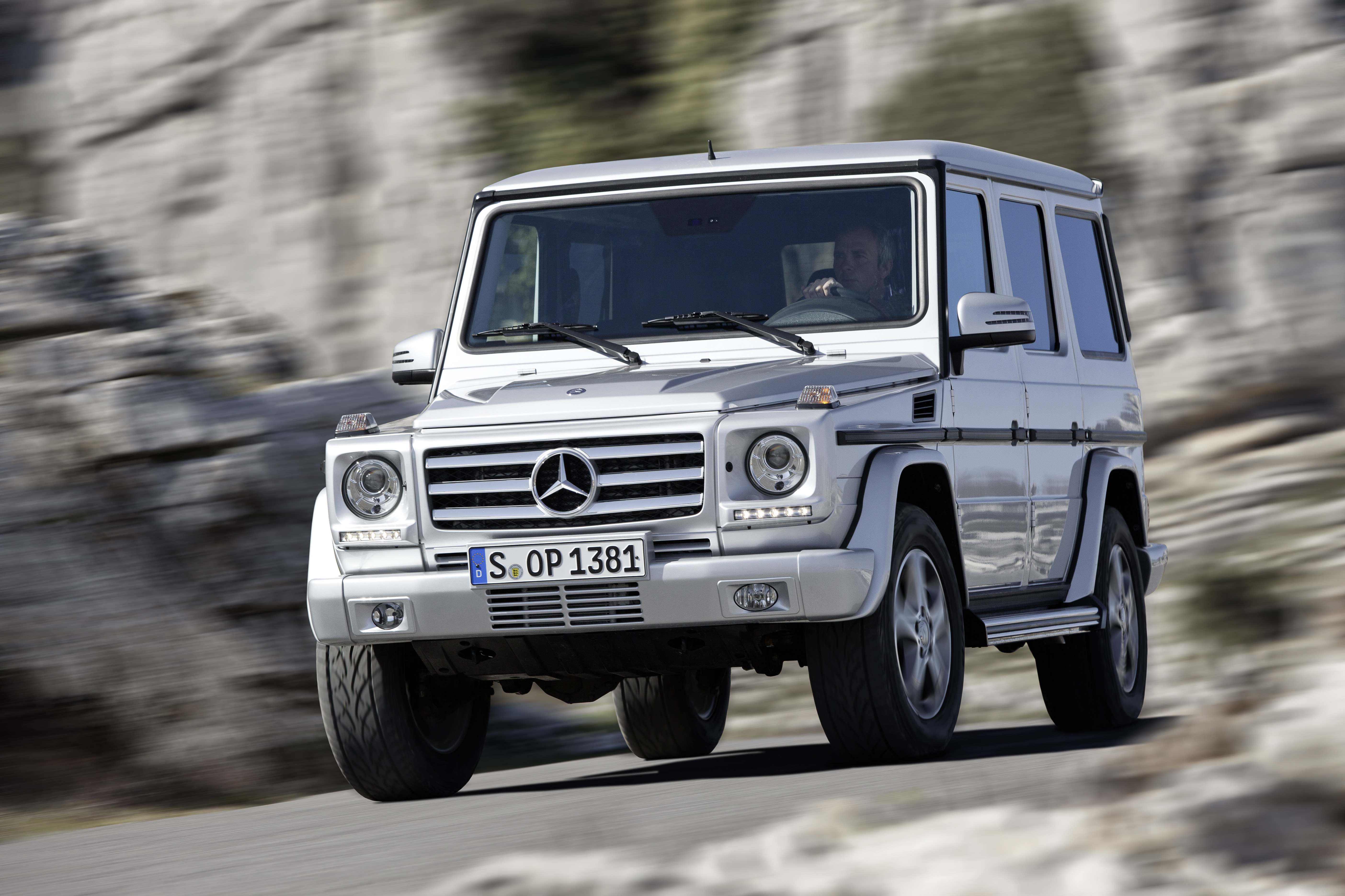 Service- und Garantiepakete | Mercedes-Benz. Eine silberne G-Klasse von Mercedes-Benz in Bewegung vor einer steinernen Felswand.